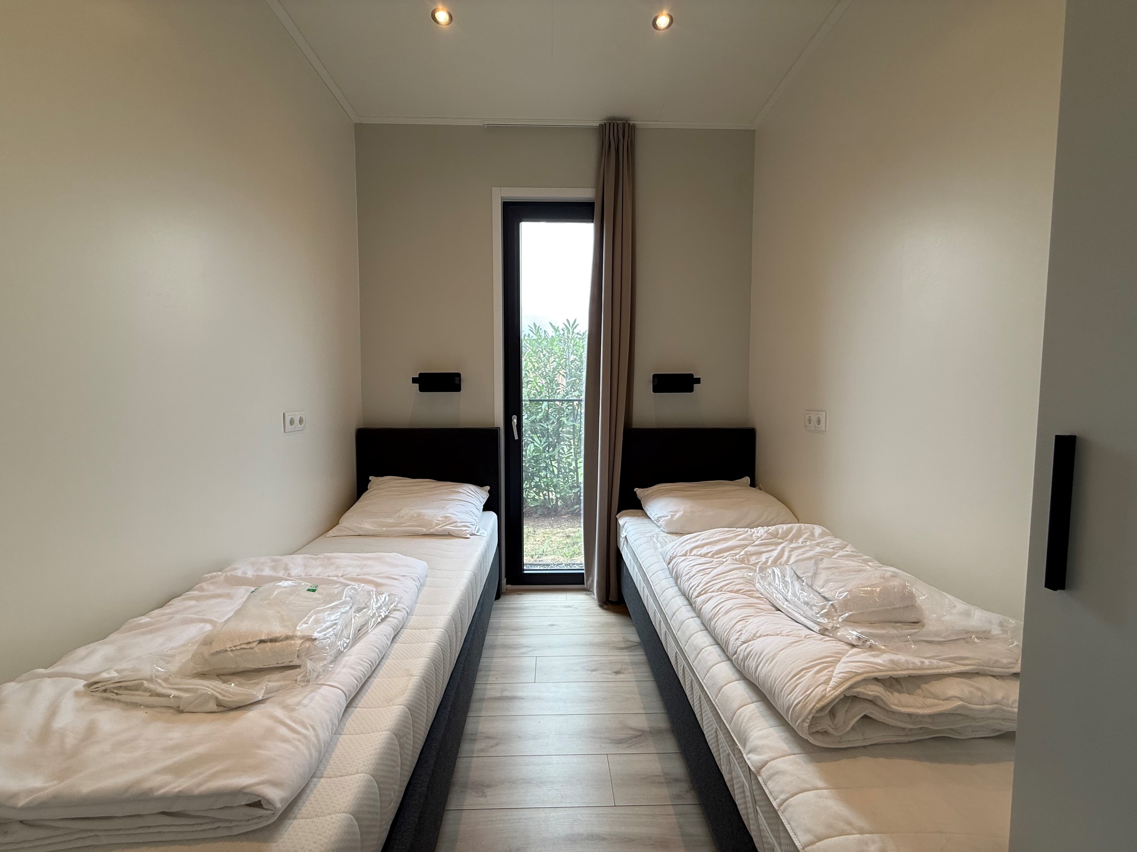 Slaapkamer met twee eenpersoonsbedden, ramen met uitzicht op de tuin en neutrale wandkleuren