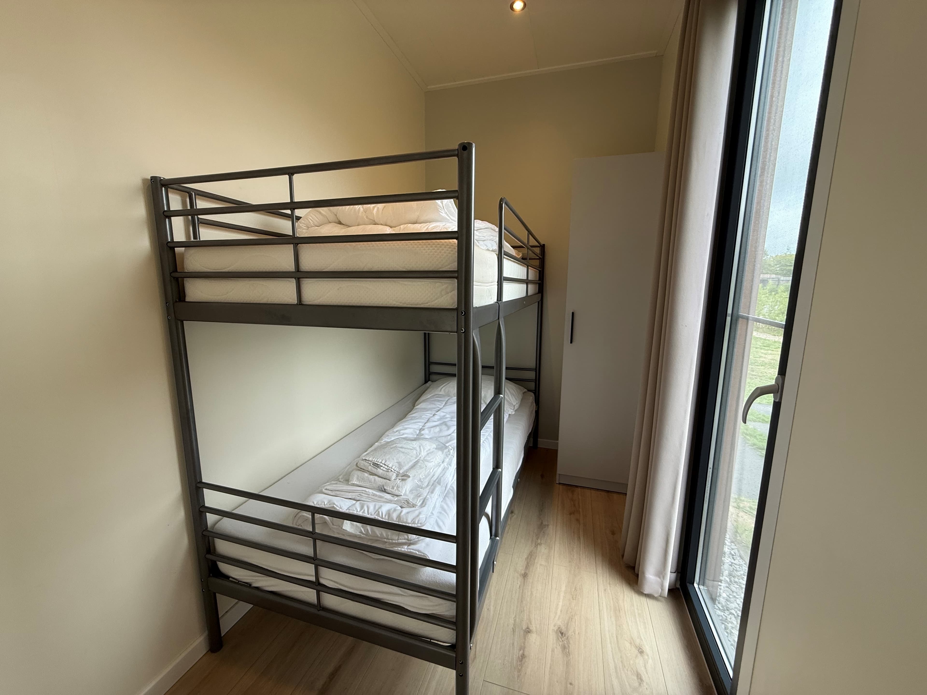 Slaapkamer met stapelbed en grote kast, veel natuurlijk licht door de ramen.