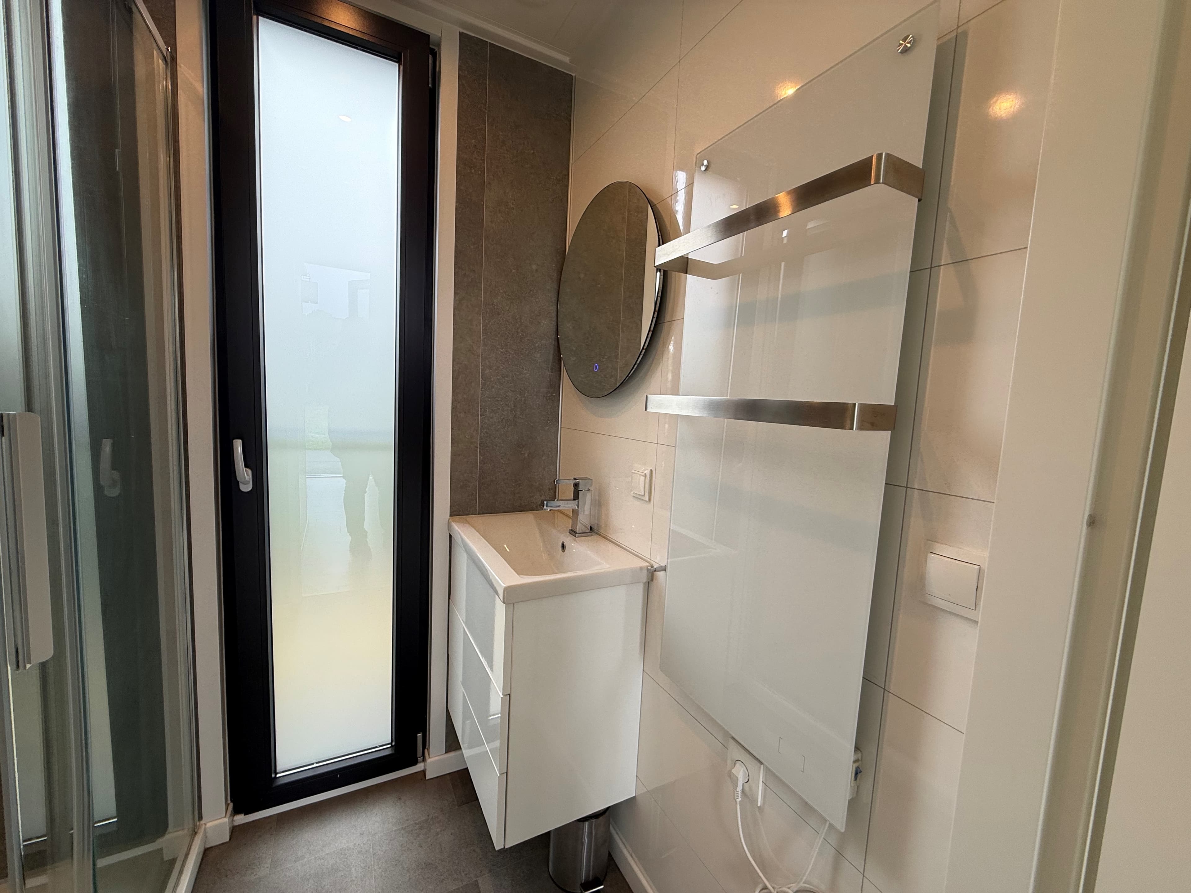 Moderne badkamer met inloopdouche, wastafelmeubel en grote spiegel, grote glazen deur naar buiten zichtbaar