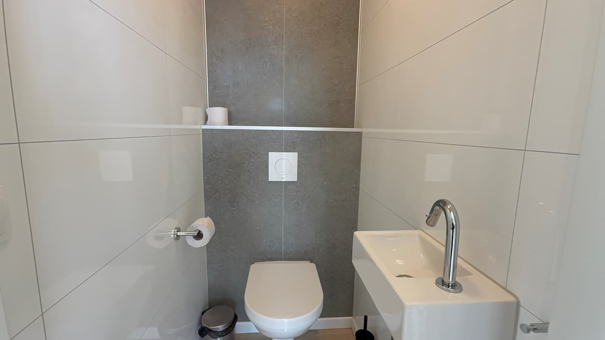 Modern toilet met wandtegels, een wastafel en een handdoekhouder in neutrale kleuren.