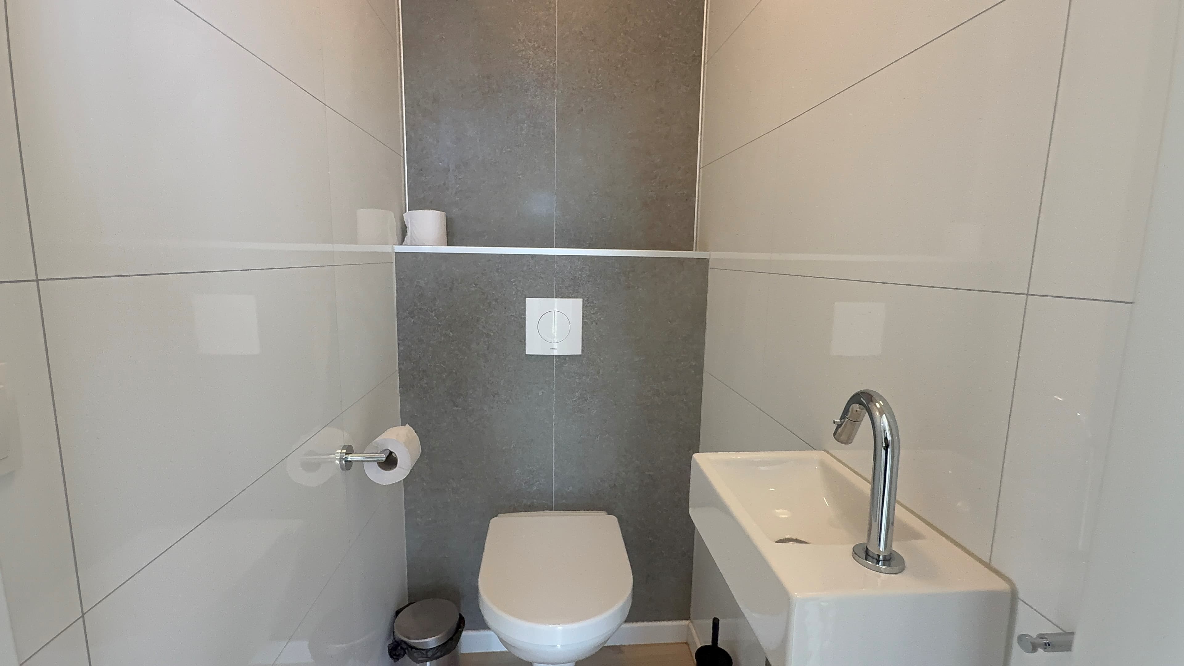 Modern toilet met wandtegels, een wastafel en een handdoekhouder in neutrale kleuren.