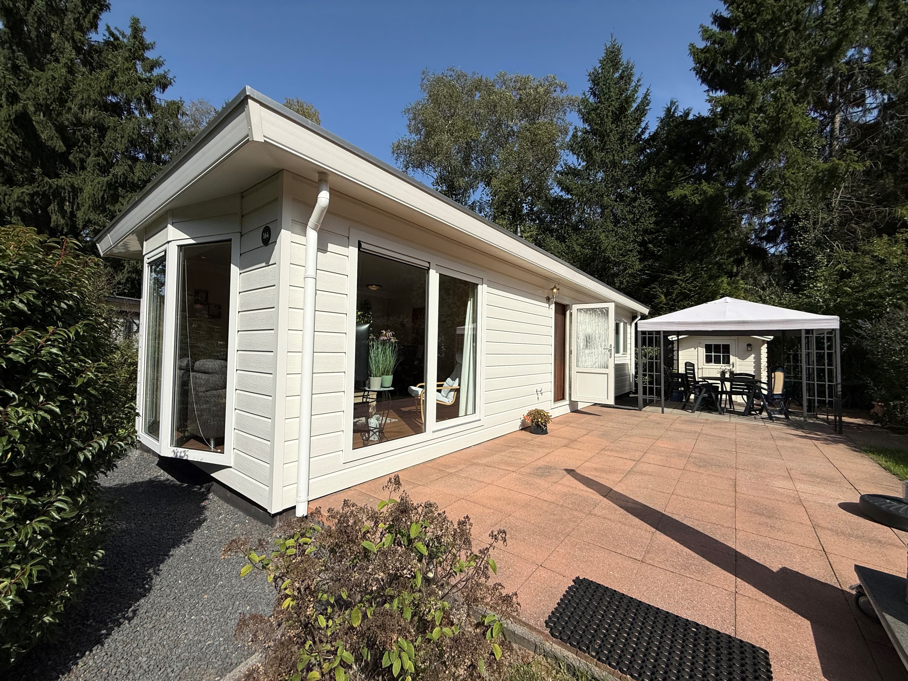 Moderne recreatiewoning met terras en overkapping, omgeven door groen en met grote ramen aan de voorzijde.
