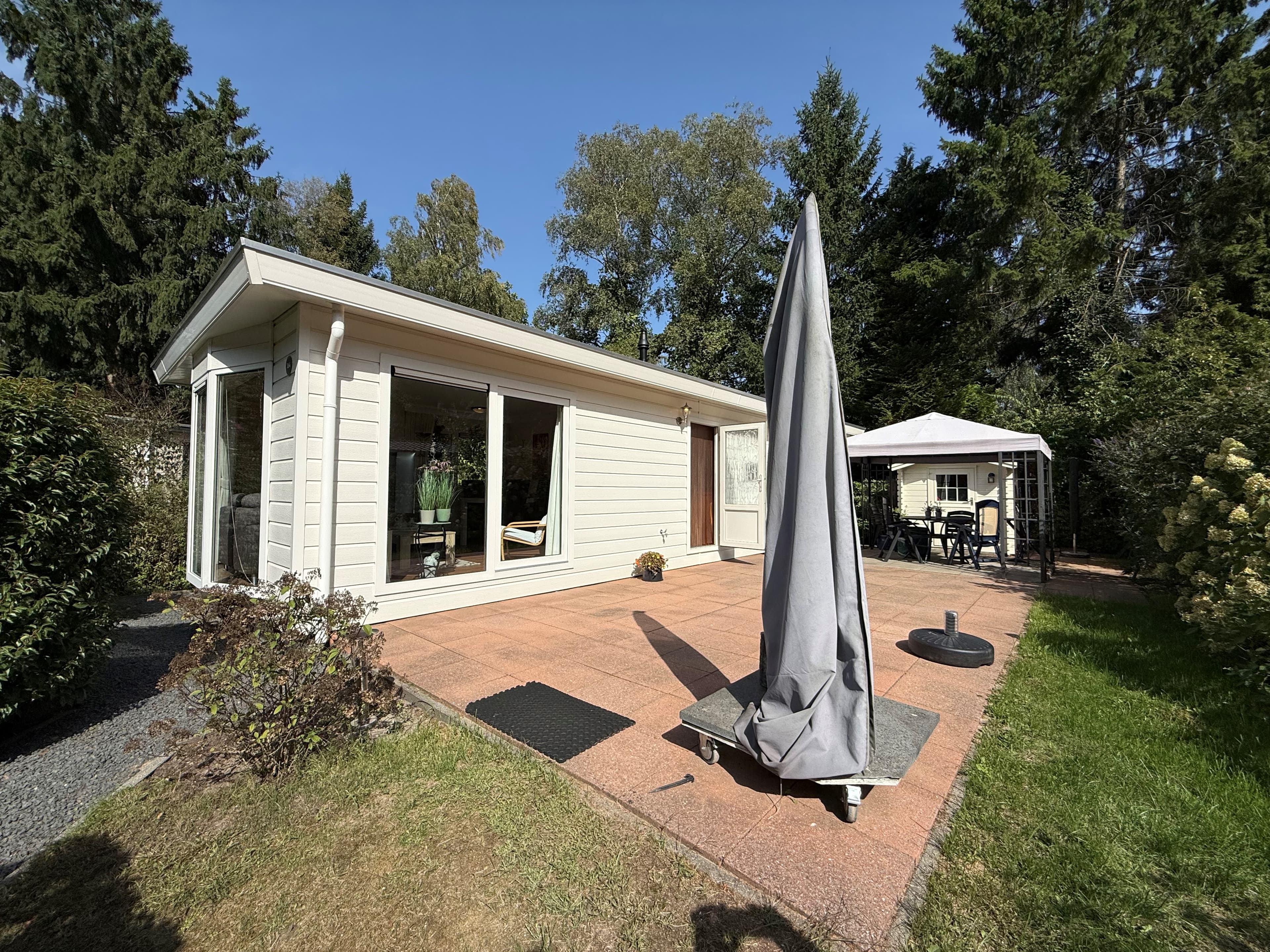 Moderne recreatiewoning met terras, omringd door groen en met een grote parasol in de tuin.