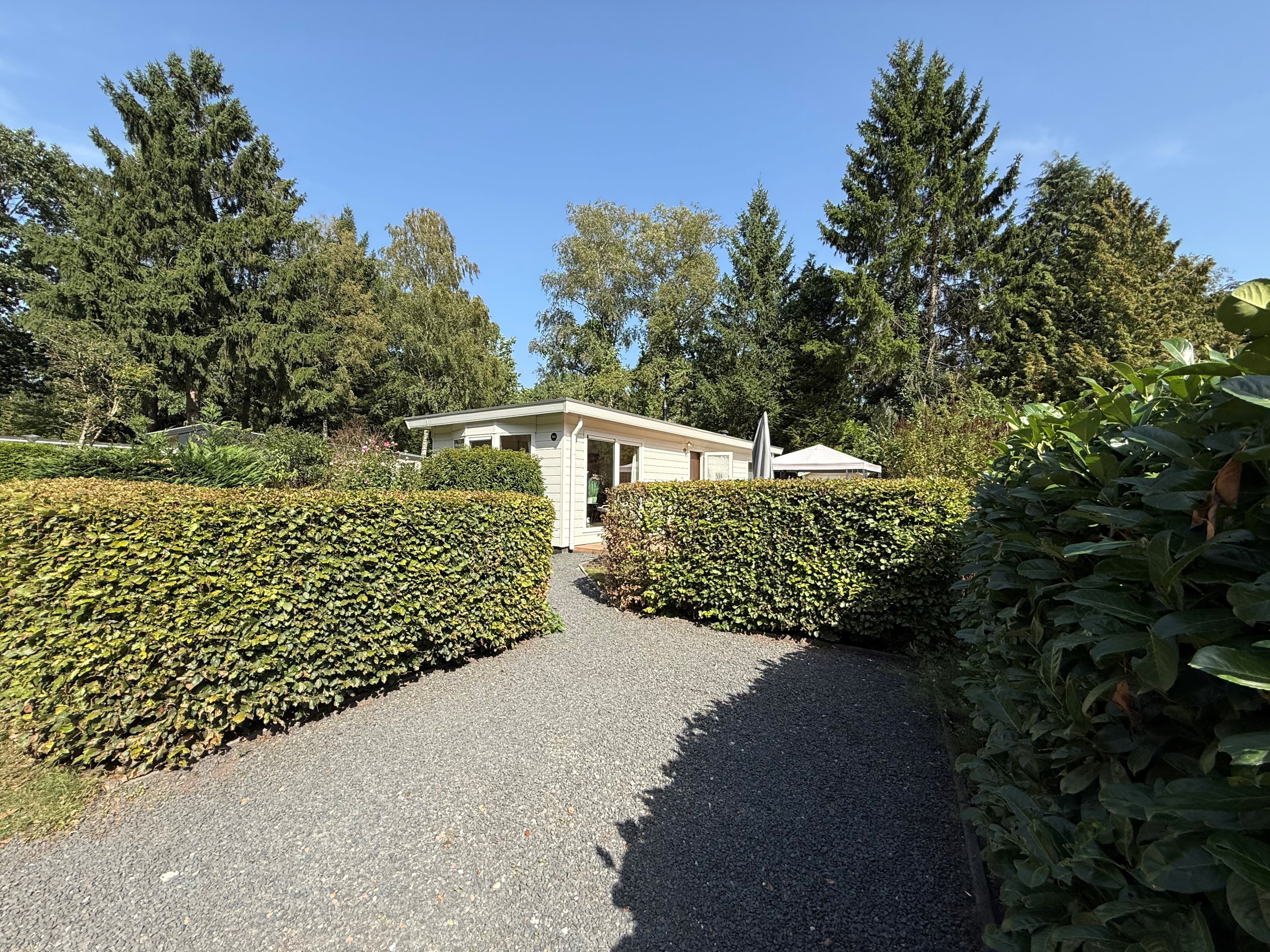 Recreatiewoning met een sierlijke tuinweg omgeven door groene heggen en bomen op een zonnige dag.