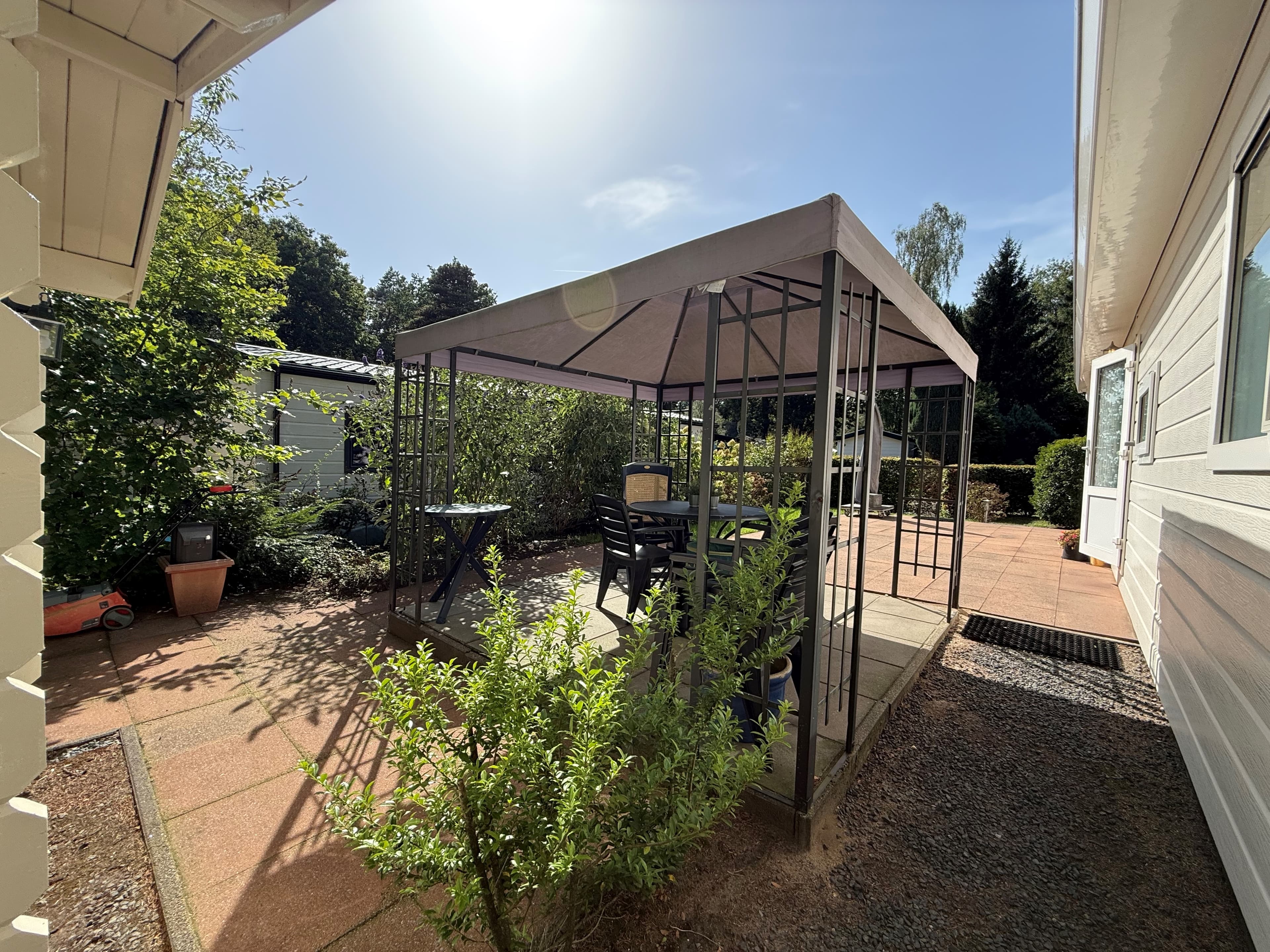 Tuin met een overkapping, met zitmeubels en omringd door groen, nabij een recreatiewoning in Ede.