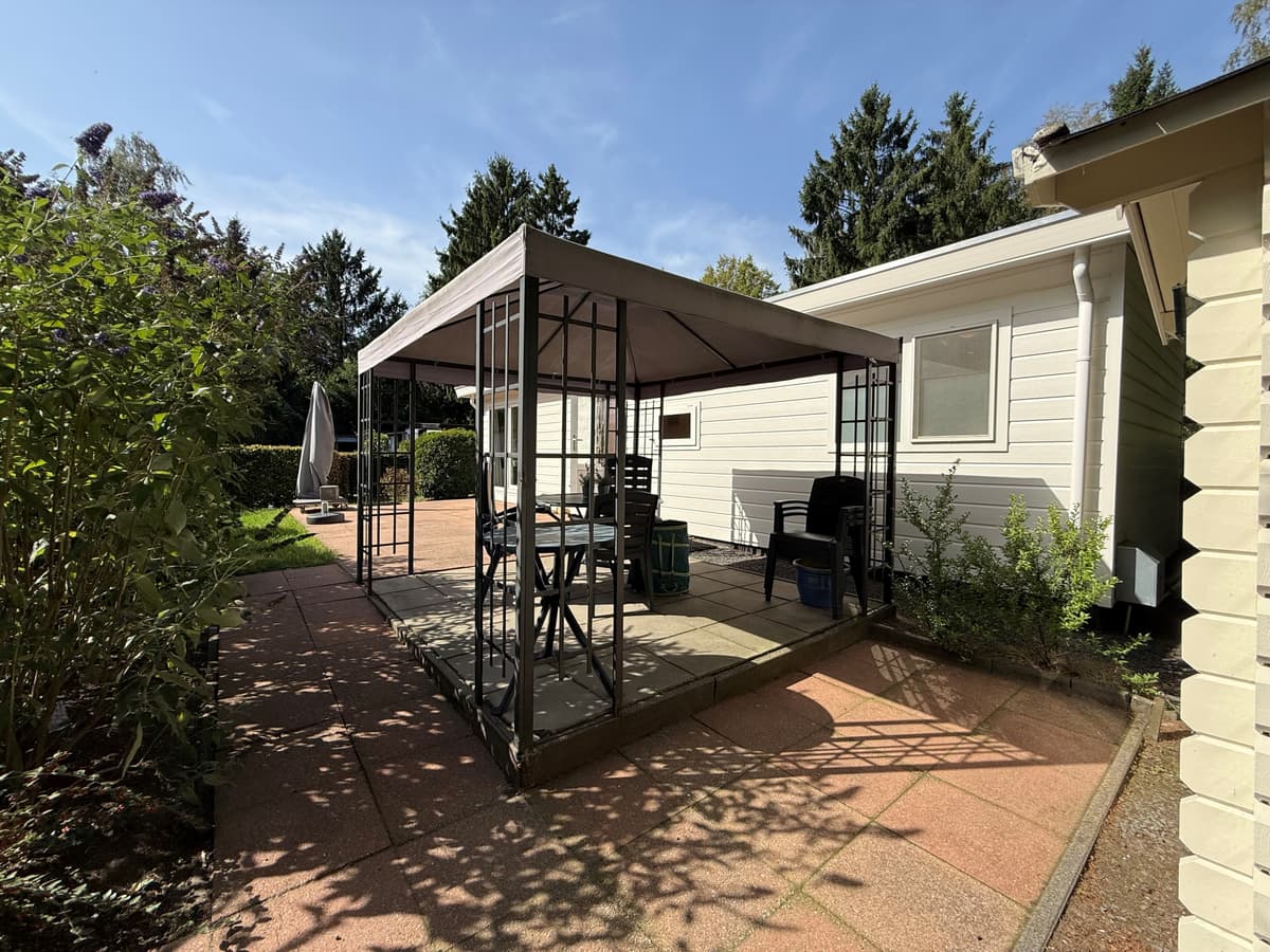 Terras met overkapping, grasstrook en omringend groen bij een recreatiewoning in Ede.