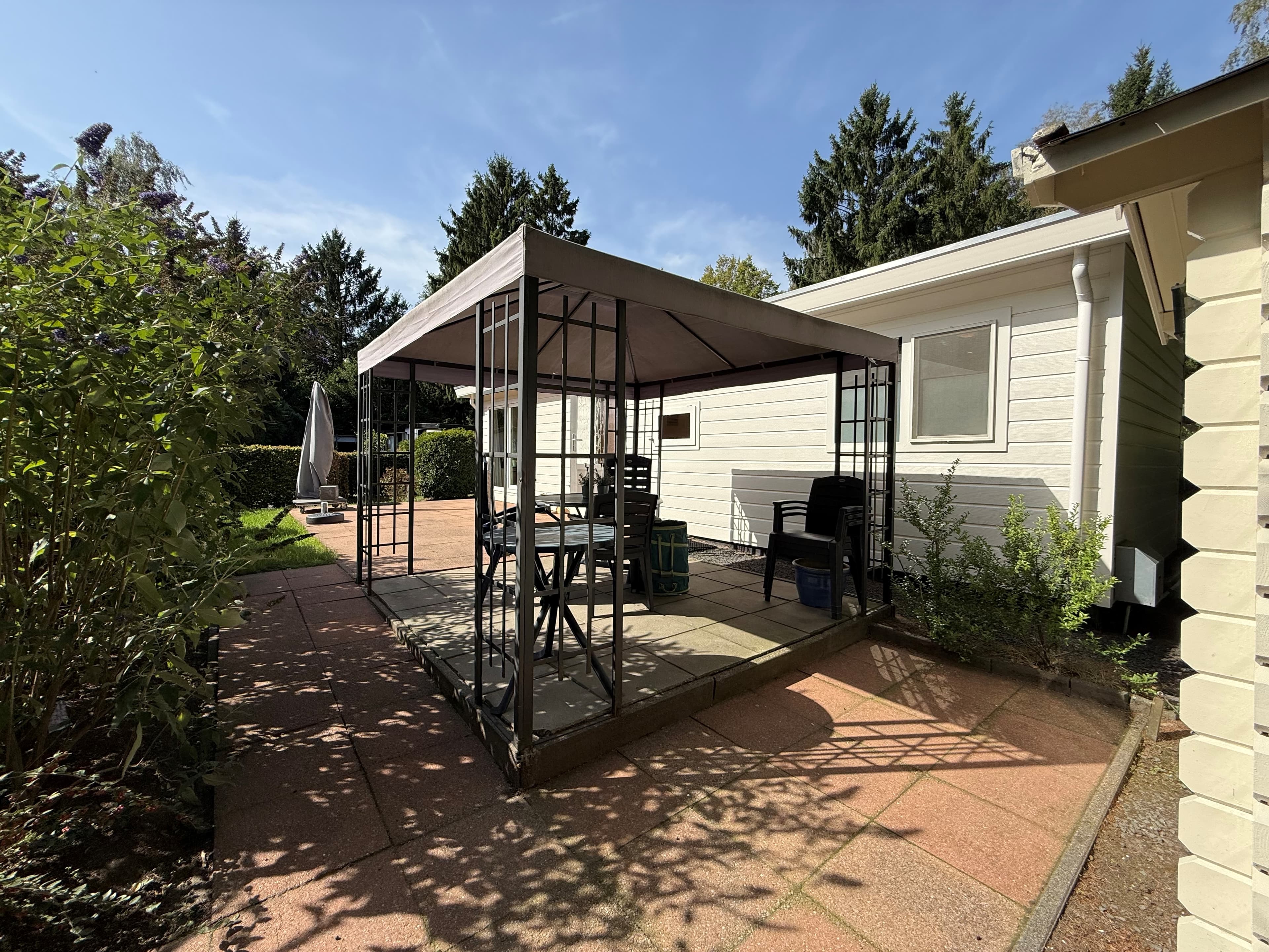 Terras met overkapping, grasstrook en omringend groen bij een recreatiewoning in Ede.