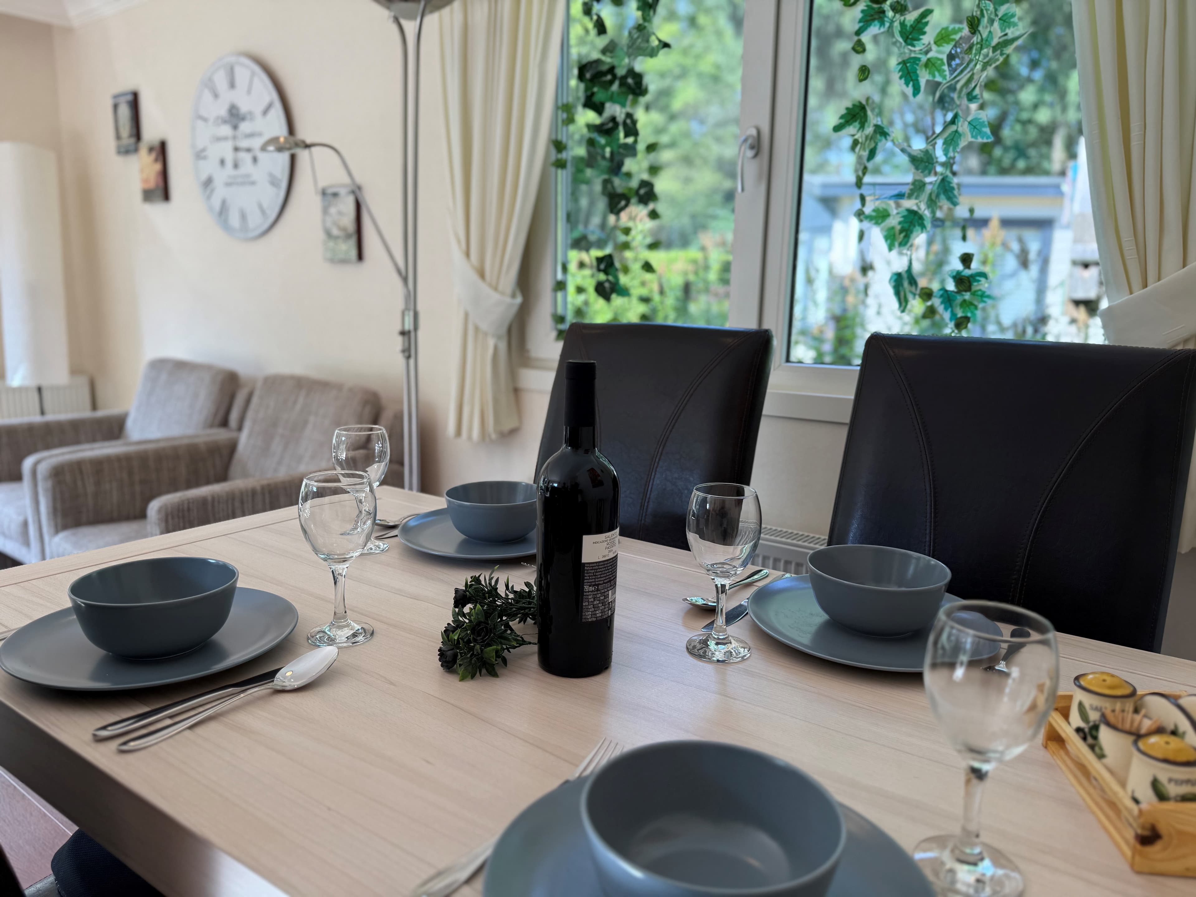 Eetkamer met een gedekte tafel, vier stoelen, een fles wijn en uitzicht op de tuin door het raam