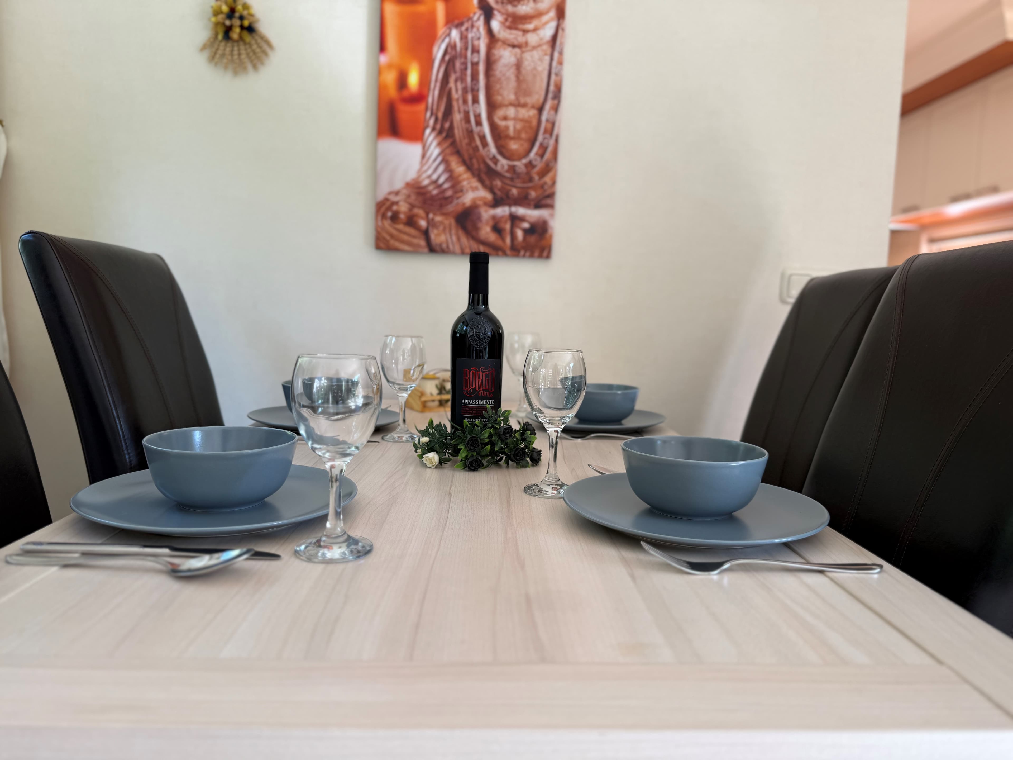 Eetkamertafel met vier borden en glazen, omringd door donkere stoelen, met een decoratieve fles in het midden