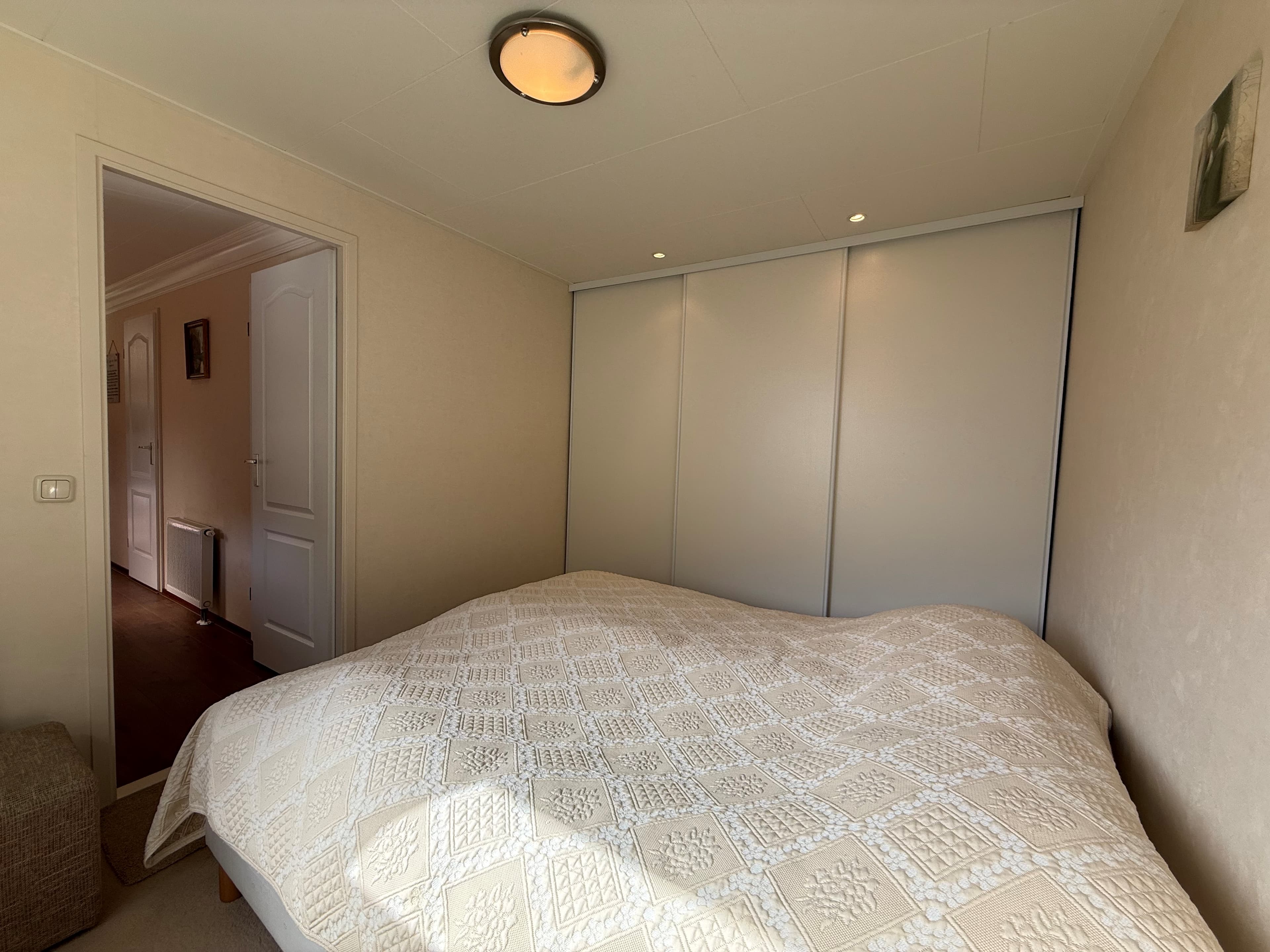 Slaapkamer met een tweepersoonsbed en toegang tot een hal met deur naar een andere kamer.