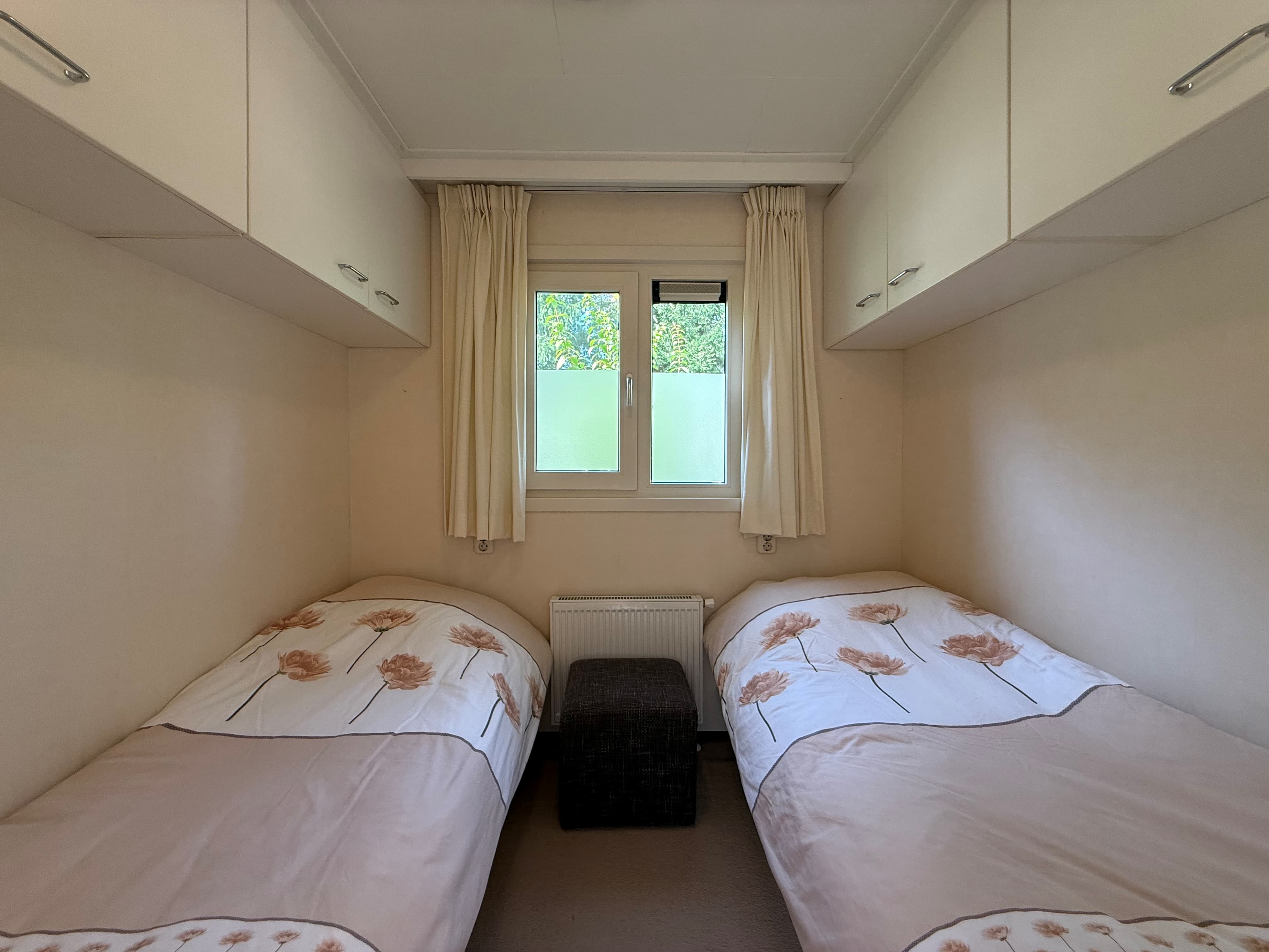 Slaapkamer met twee eenpersoonsbedden en een klein meubel in het midden, gordijnen voor het raam