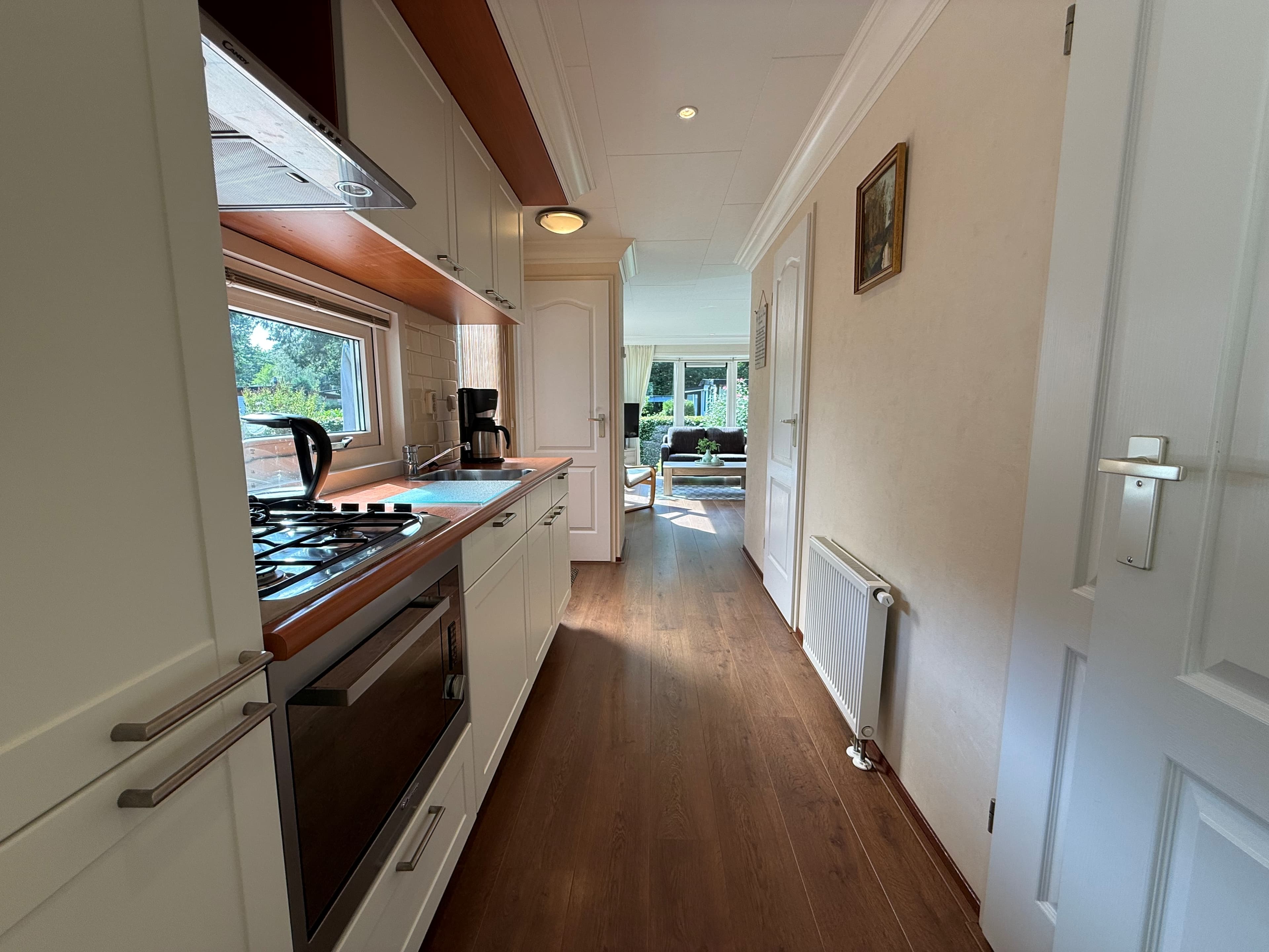 Modelkeuken met moderne apparatuur en lichtinval, leidt naar een woonruimte met een zithoek en veel natuurlijk licht