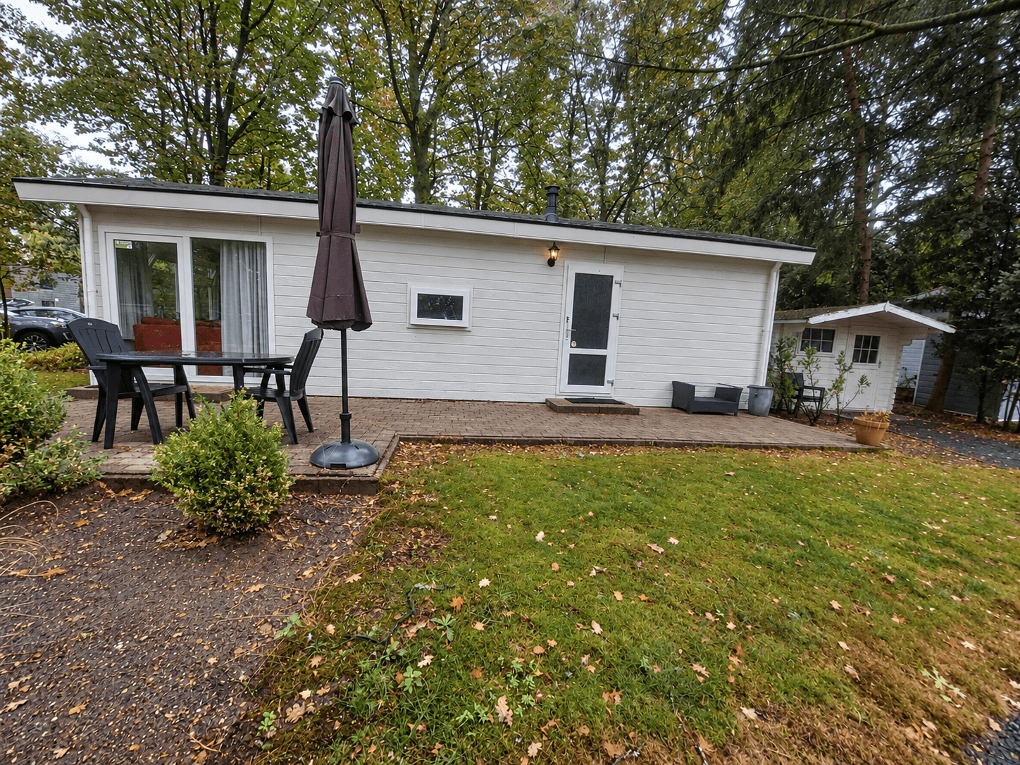Recreatiewoning met een terras, tuinstoelen en een markies, omgeven door gras en bomen in een rustige omgeving.
