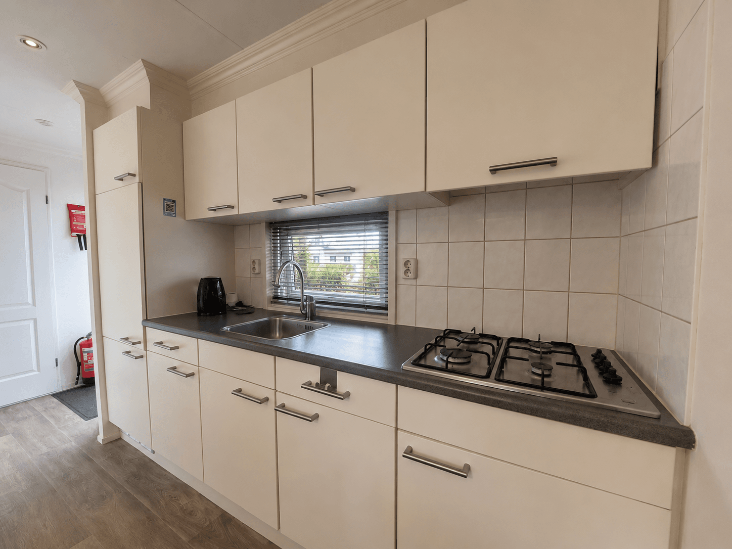 Keuken met inbouwkasten, gasfornuis en spoelbak in lichte kleuren met laminaatvloer