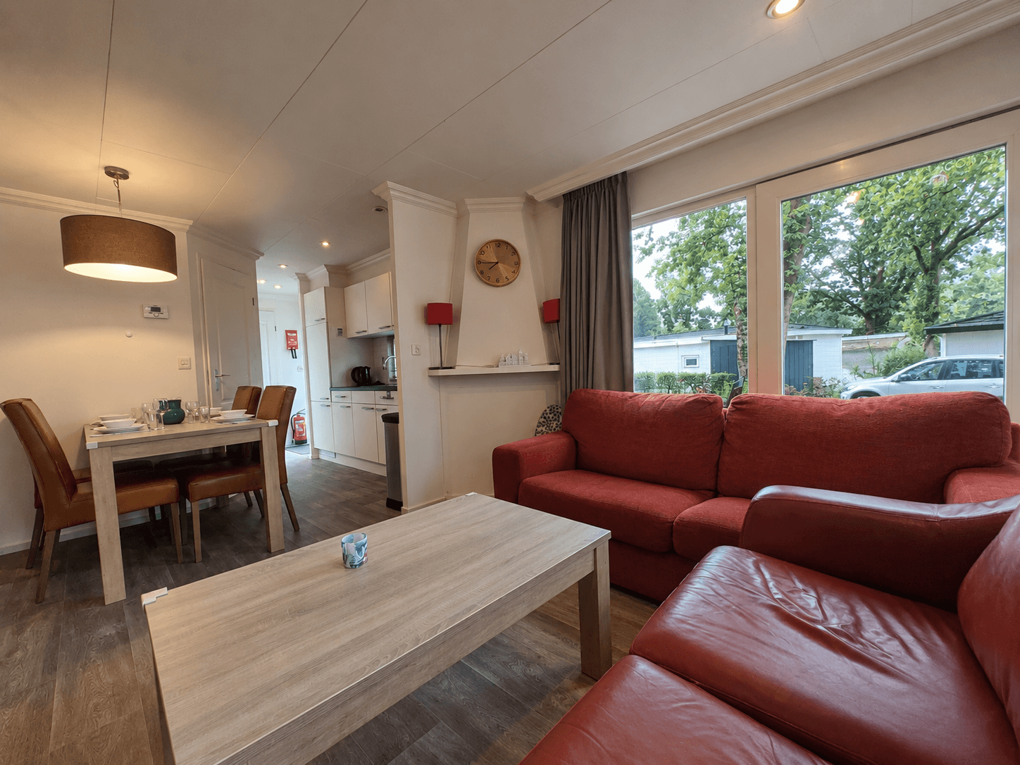 Huiselijke recreatiewoning met zithoek, eettafel en toegang tot buiten, grote ramen met uitzicht op de groene omgeving