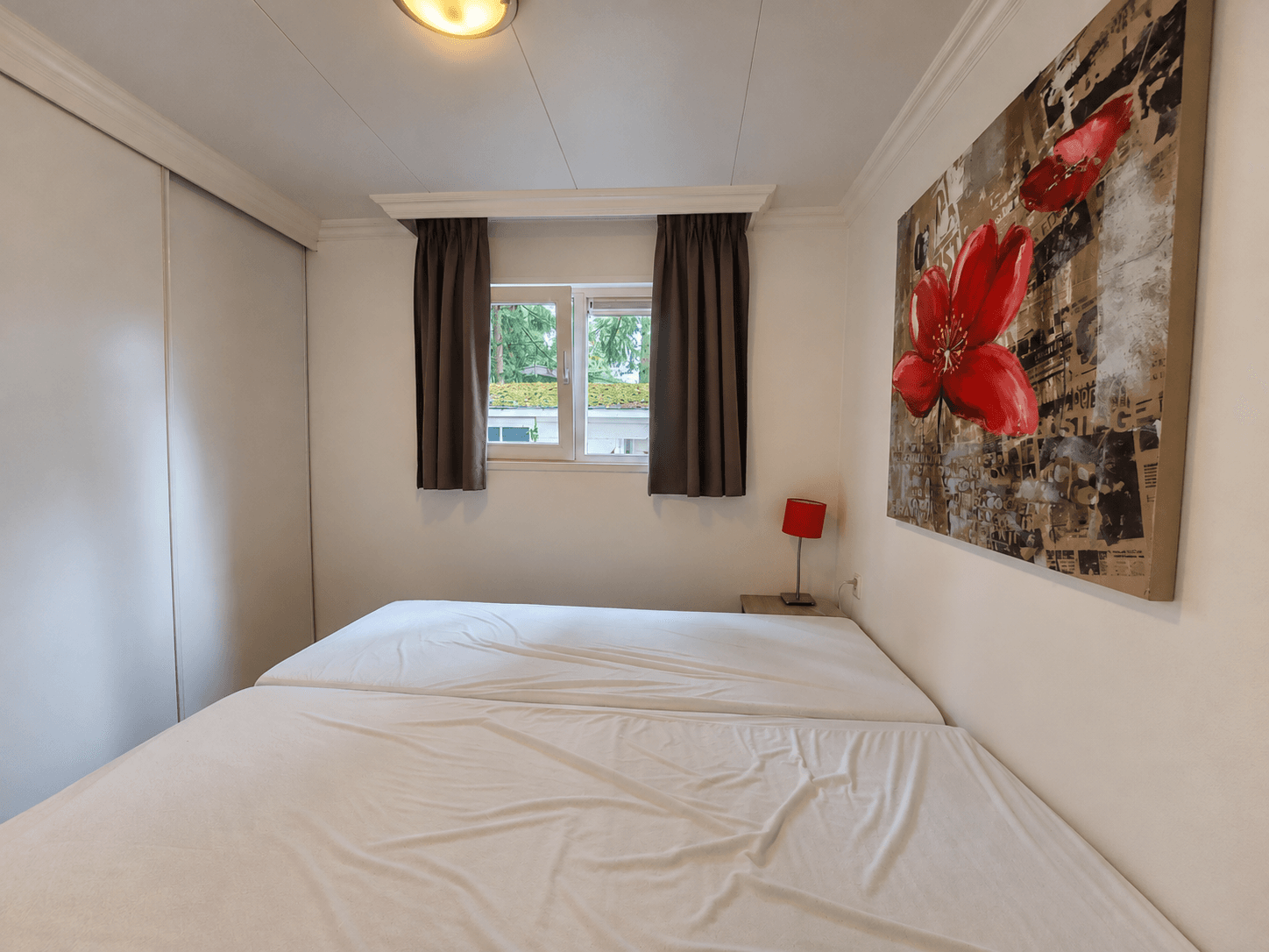 Slaapkamer met twee aparte bedden, een raam met uitzicht en een schilderij met een rode bloem aan de muur