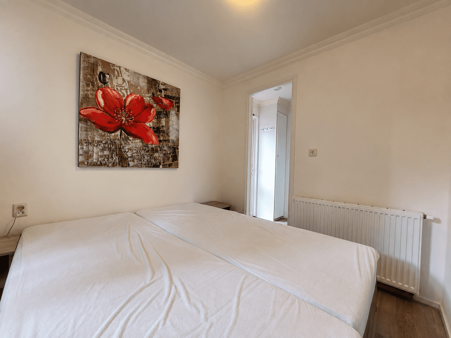 Slaapkamer met twee bedden, een schilderij van een rode bloem aan de muur en een deur naar een badkamer