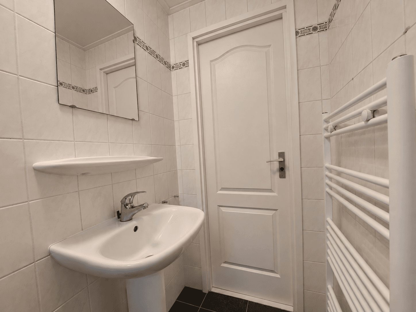 Moderne badkamer met wastafel, spiegel en handdoekradiator in lichte tegels en zwart tegelvloer