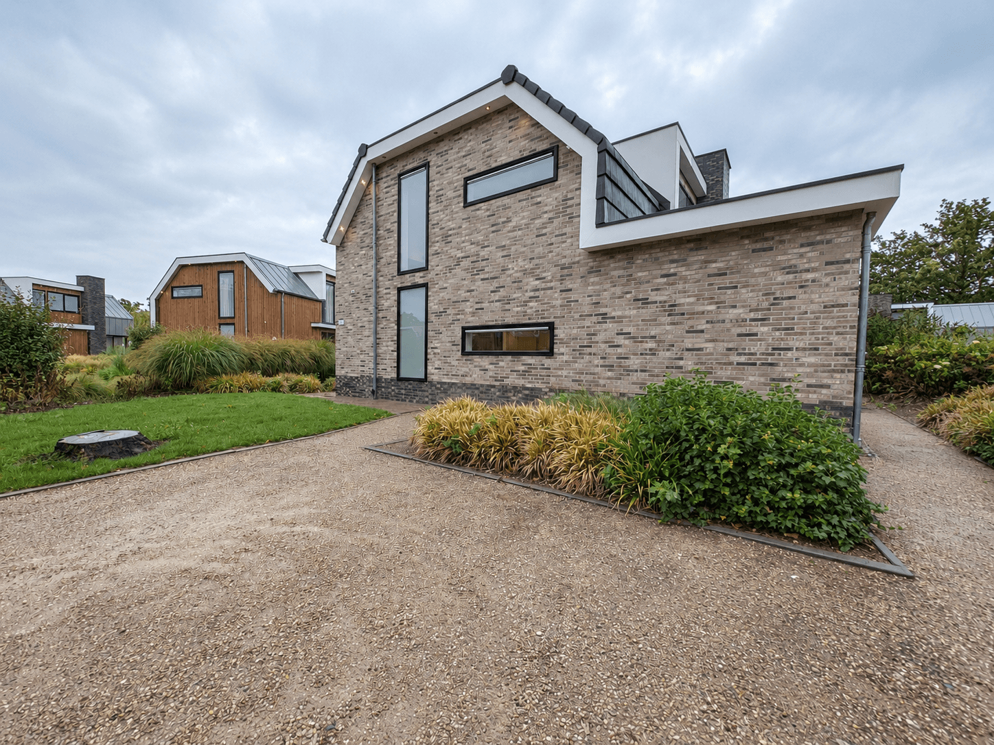 Moderne recreatiewoning met gevel van steen, groene planten rondom en grindpad in EuroParcs Zuiderzee, Biddinghuizen