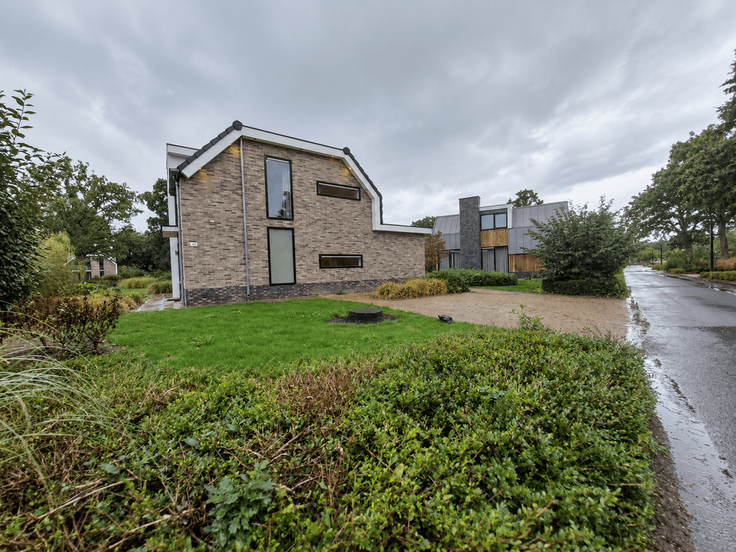 Moderne recreatiewoning met stenen gevel, grote ramen en een tuin met gras en planten aan een rustige straat