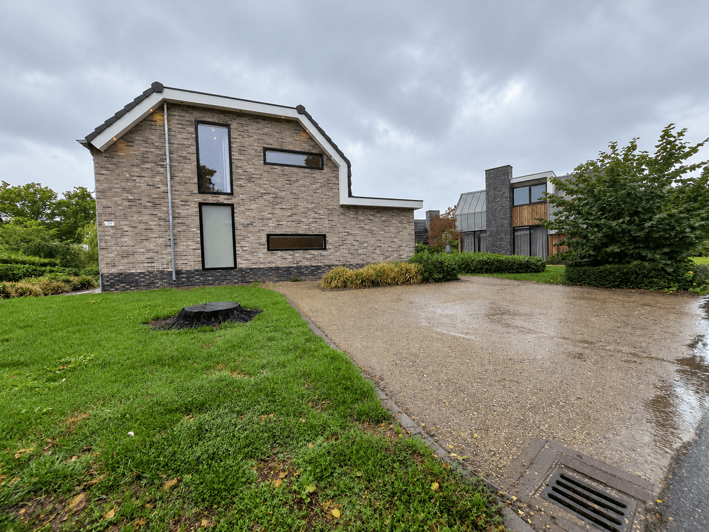Moderne recreatiewoning met stenen gevel en grote ramen, omgeven door groen gras en een grindpad.
