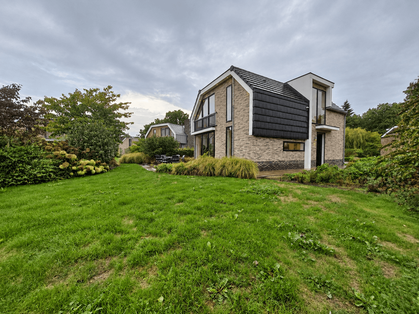 Tuin en moderne recreatiewoning met een mix van baksteen en zwarte gevelbekleding in een groene omgeving