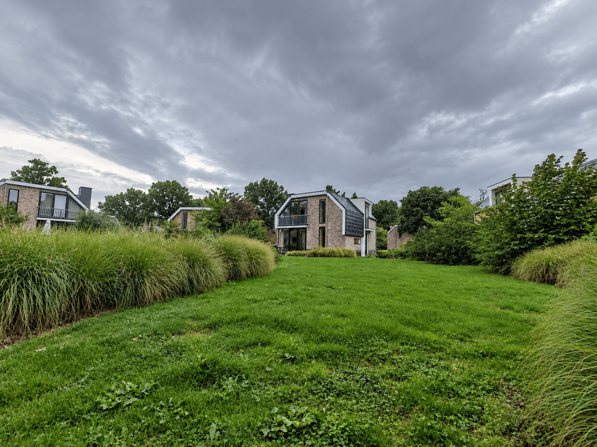 Recreatiewoning omringd door gras en struiken met een lichte, moderne gevel onder een bewolkte lucht.