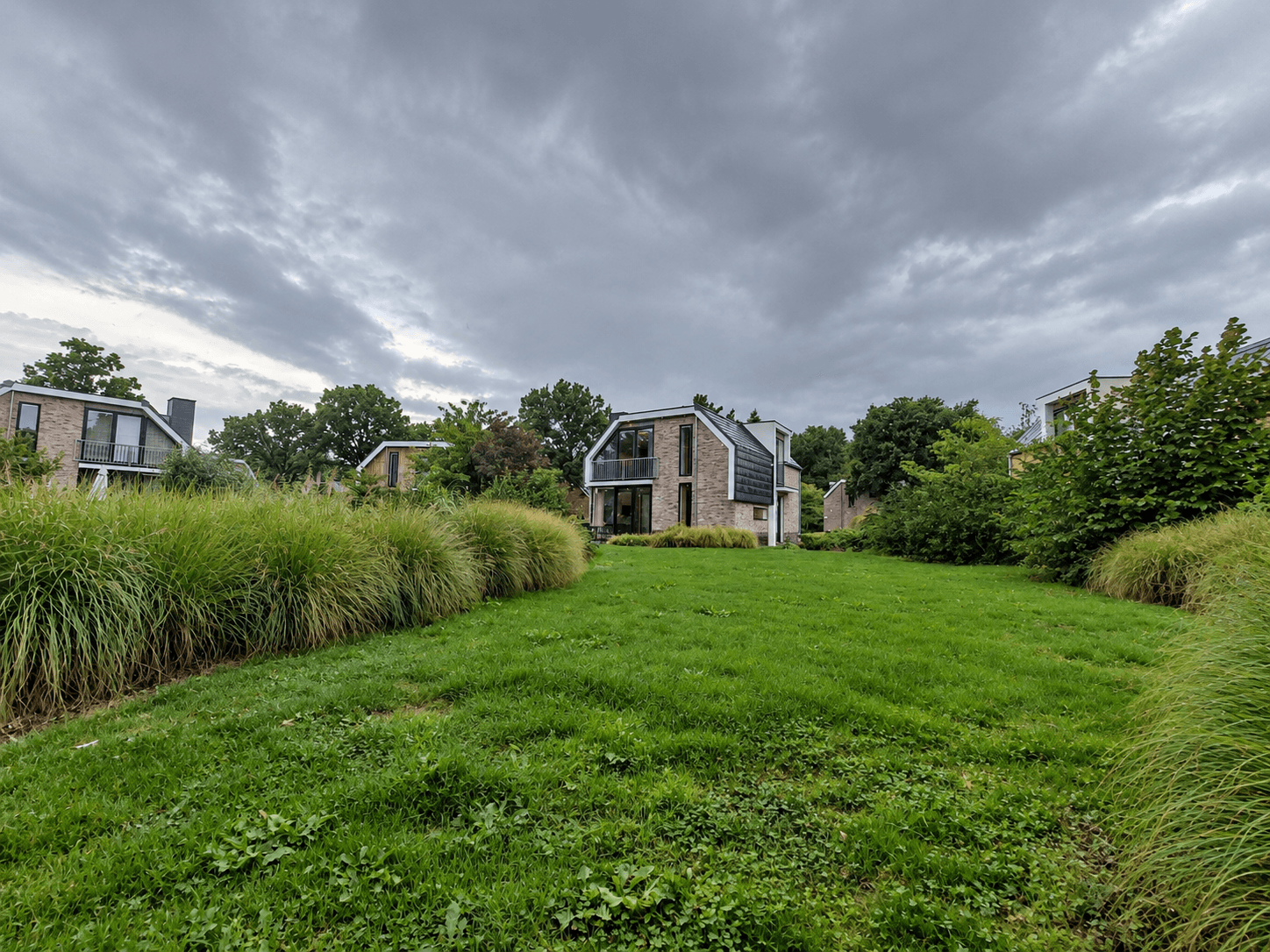 Recreatiewoning omringd door gras en struiken met een lichte, moderne gevel onder een bewolkte lucht.