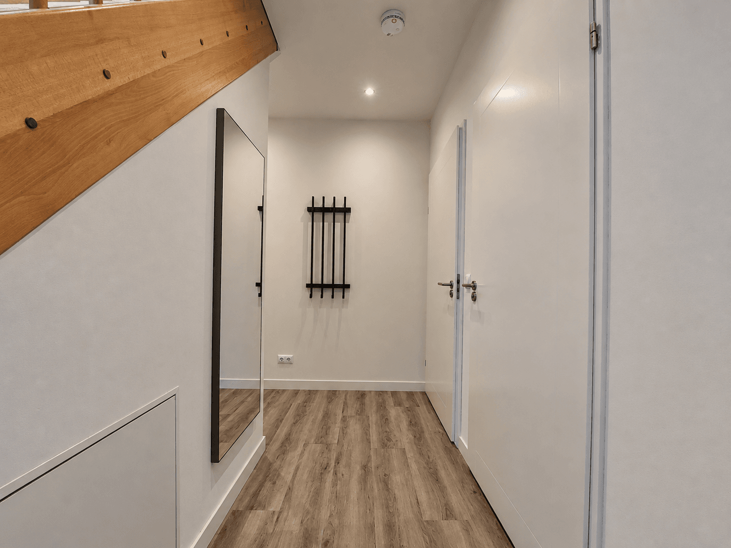 Entree van een recreatiewoning met een spiegel, wandrek en houten trap naar boven, lichte wanden en laminaatvloer