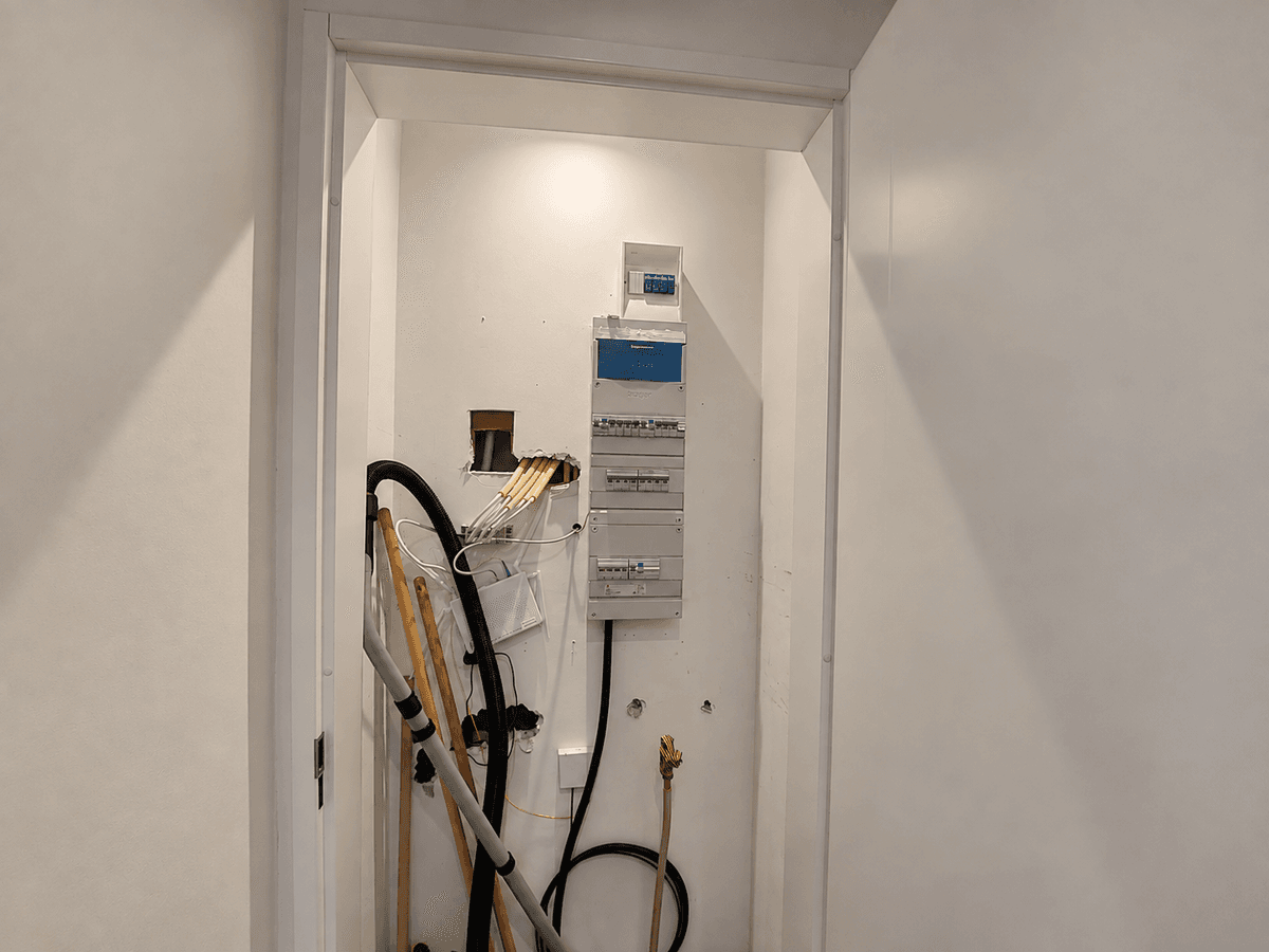 Inham met elektrische meterkast aan de muur en zichtbaar leidingwerk, en een stofzuiger in de hoek.