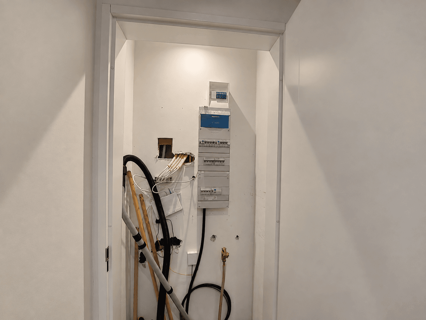 Inham met elektrische meterkast aan de muur en zichtbaar leidingwerk, en een stofzuiger in de hoek.