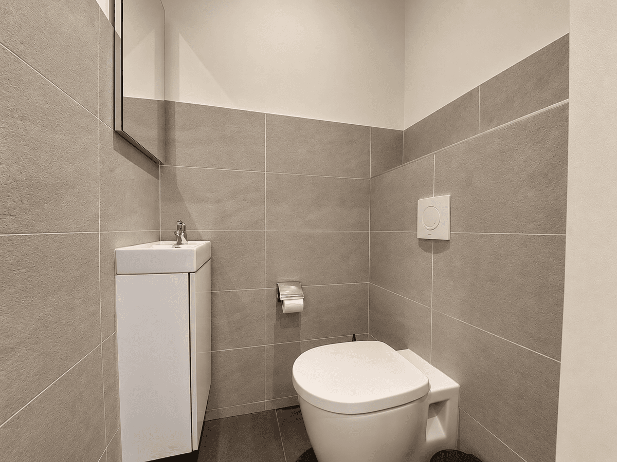 Modern toilet met beige en grijze tegels, een klein wastafeltje en een spiegel aan de muur.