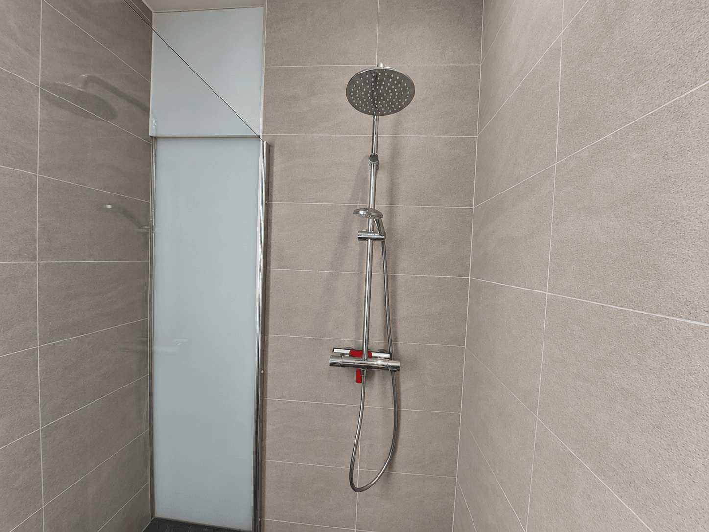 Moderne douche met ronde regendouchekop en glazen douchewand in een betegelde badkamer