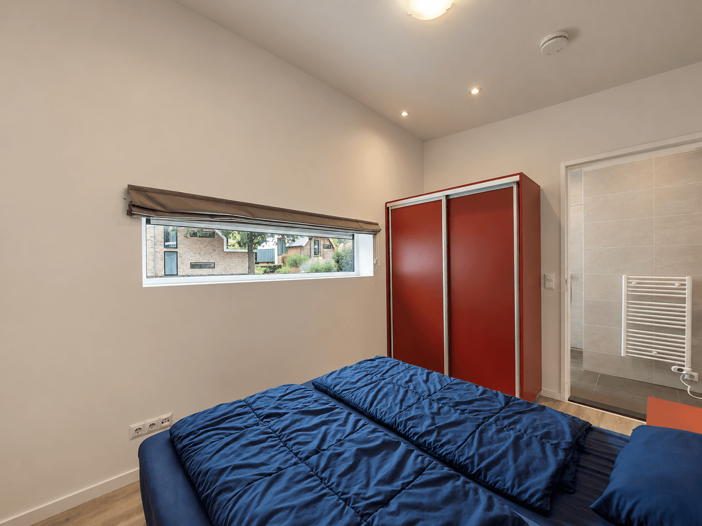 Slaapkamer met tweepersoonsbed, kleurrijke kast en raam met uitzicht op buiten.