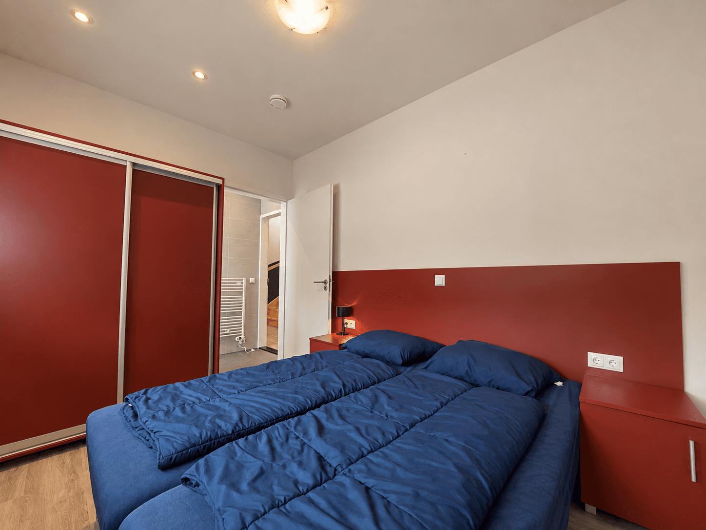 Slaapkamer met twee eenpersoonsbedden, rode kastenwand en verlichting aan het plafond.