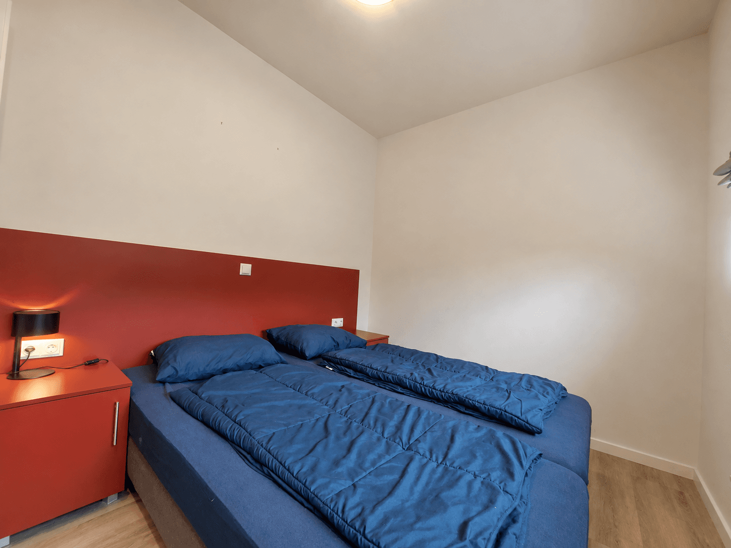 Slaapkamer met twee eenpersoonsbedden en een nachtkastje tegen een wand in een rustige kleurstelling