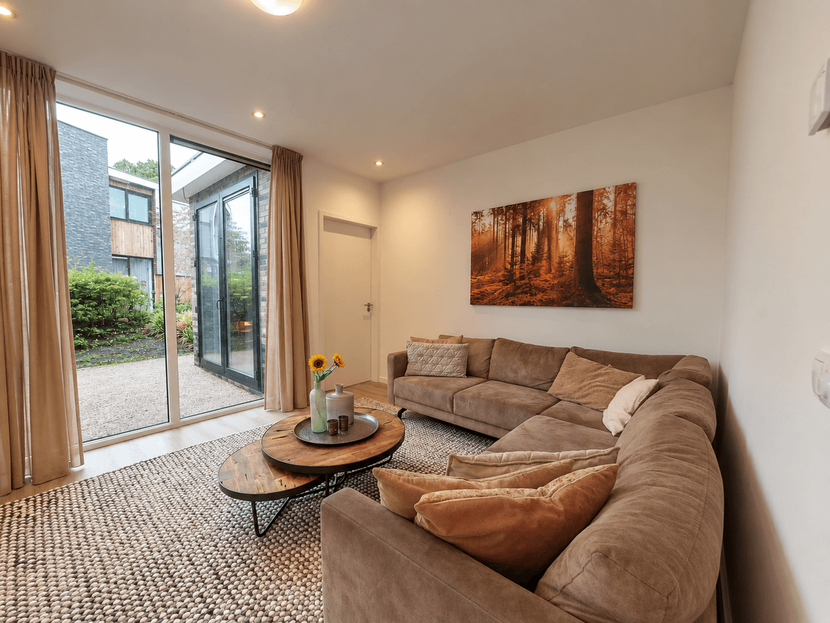 Moderne woonkamer met een loungebank, een salontafel en grote ramen die uitkijken op de tuin