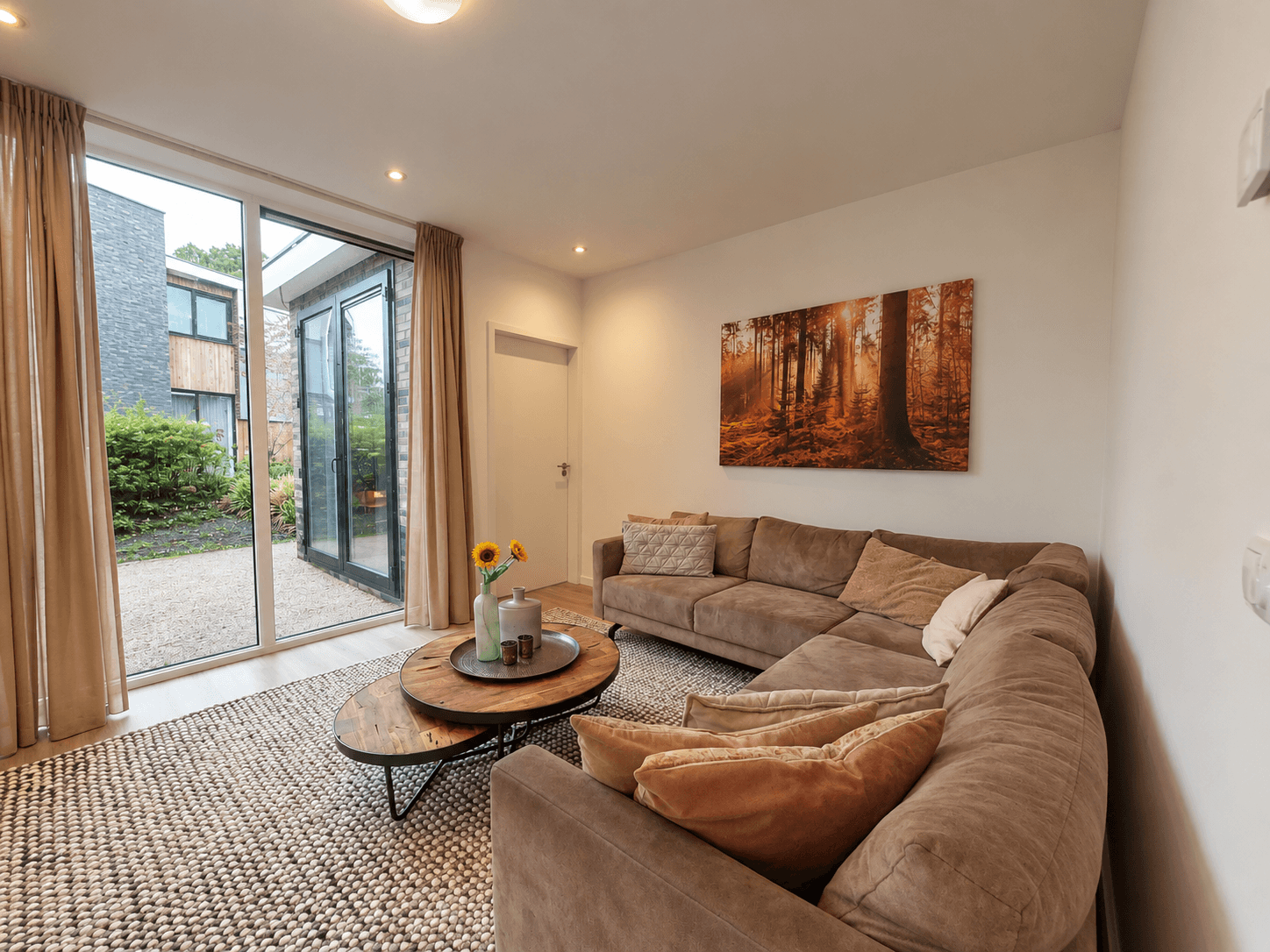 Moderne woonkamer met een loungebank, een salontafel en grote ramen die uitkijken op de tuin