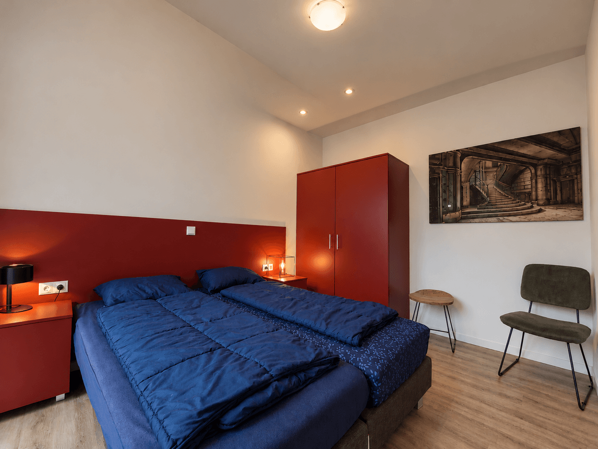 Slaapkamer met twee eenpersoonsbedden, rode wanden, kast en een stoel tegen een lichte muur.