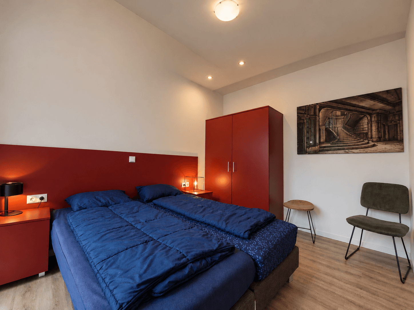 Slaapkamer met twee eenpersoonsbedden, rode wanden, kast en een stoel tegen een lichte muur.