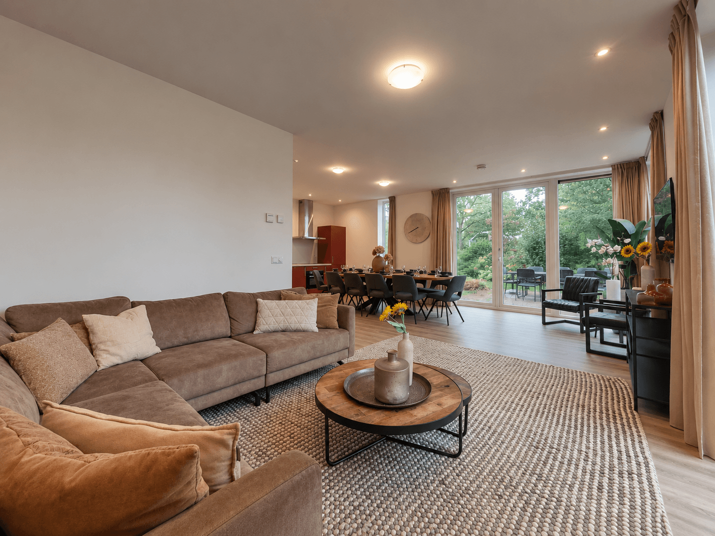 Woonkamer met een comfortabele loungebank, eettafel en grote ramen met uitzicht op de tuin.