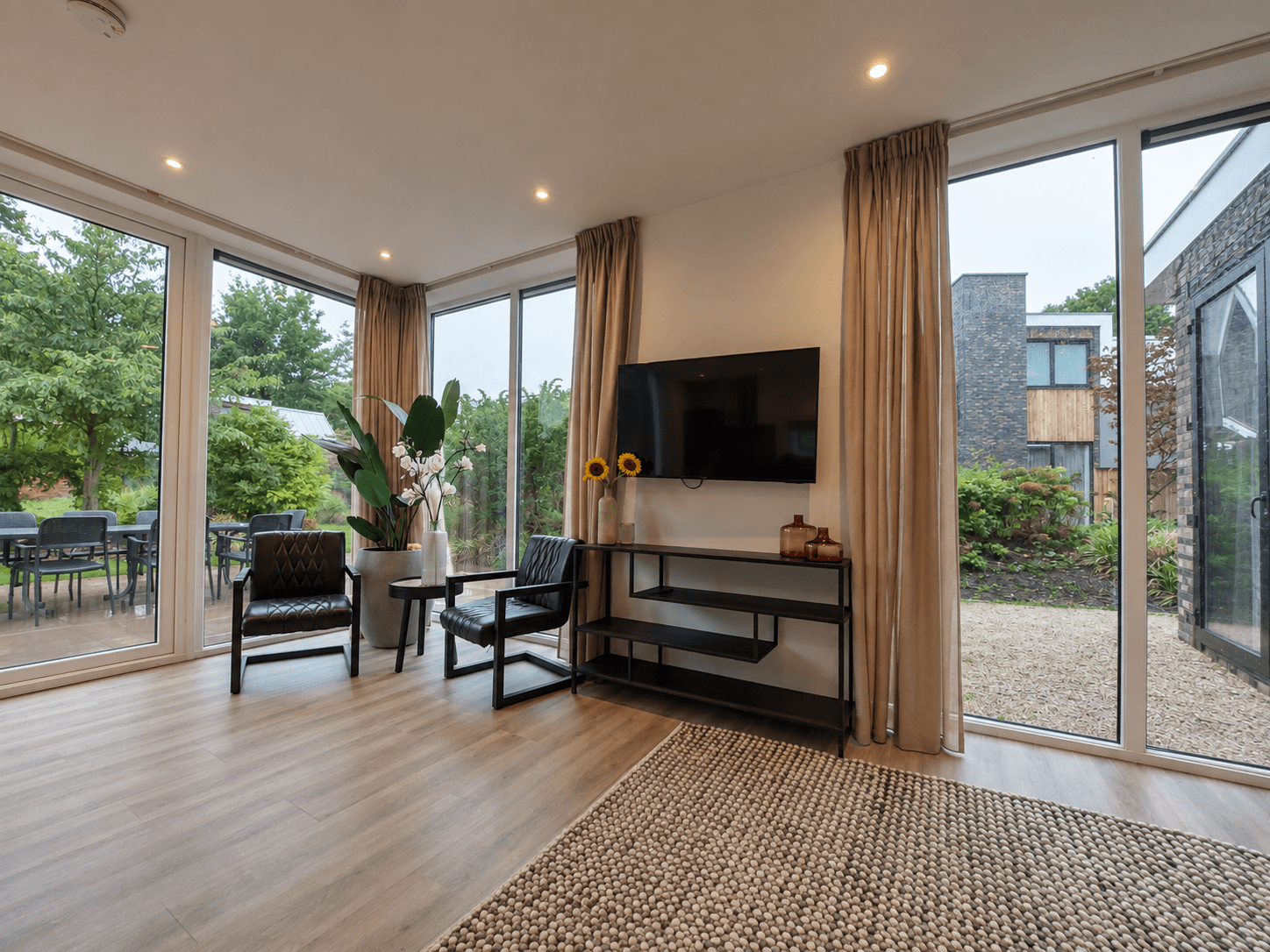 Hedendaagse woonkamer met grote ramen, zwart-witte stoelen en een tv-meubel, uitzicht op een groen buitengebied