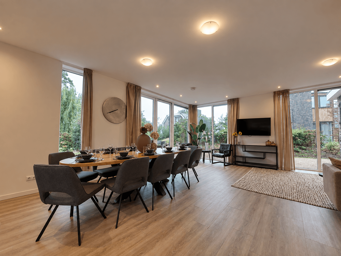Eetkamer met een lange tafel, stoelen en een zithoek met tv en raam met uitzicht op de tuin