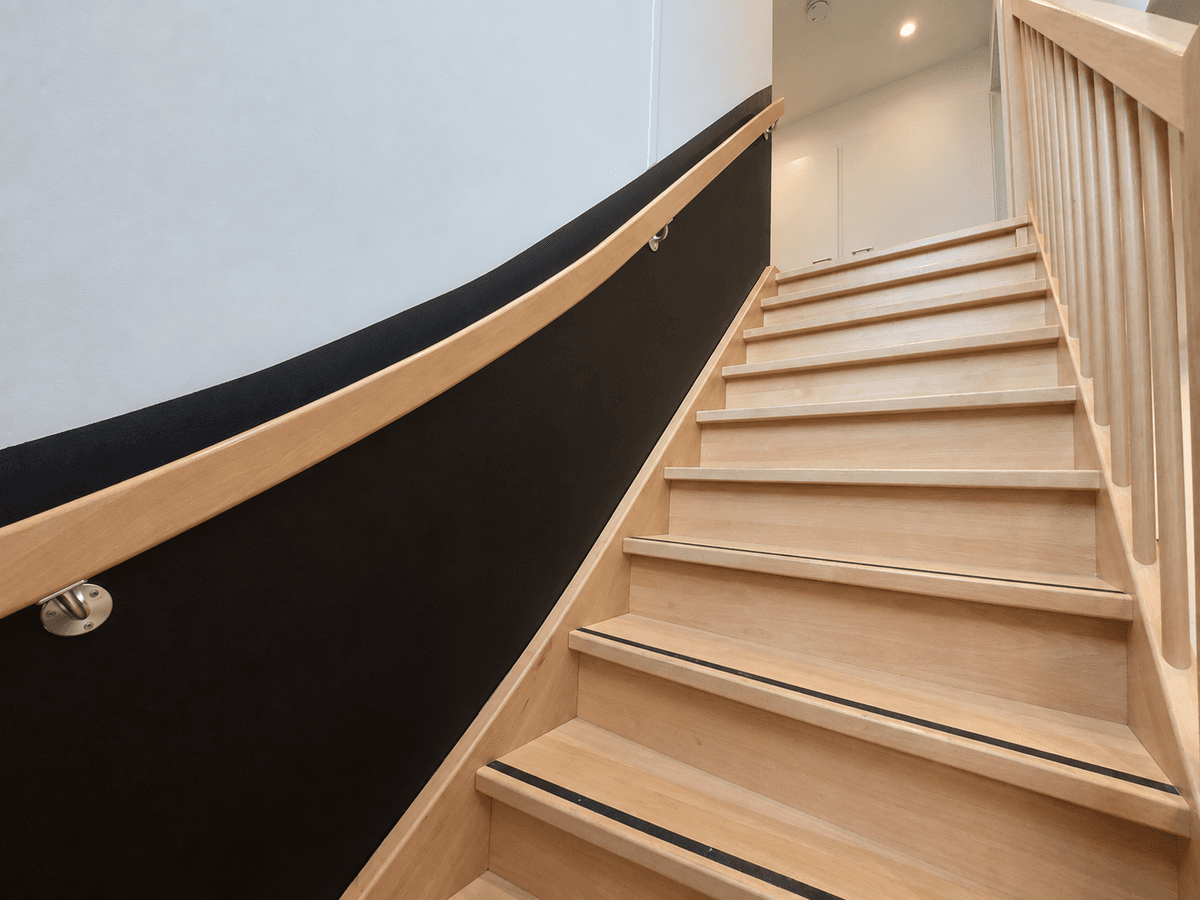 Houten trap met lichte treden en zwart afgeronde leuning, leidt naar de bovenverdieping van de recreatiewoning.