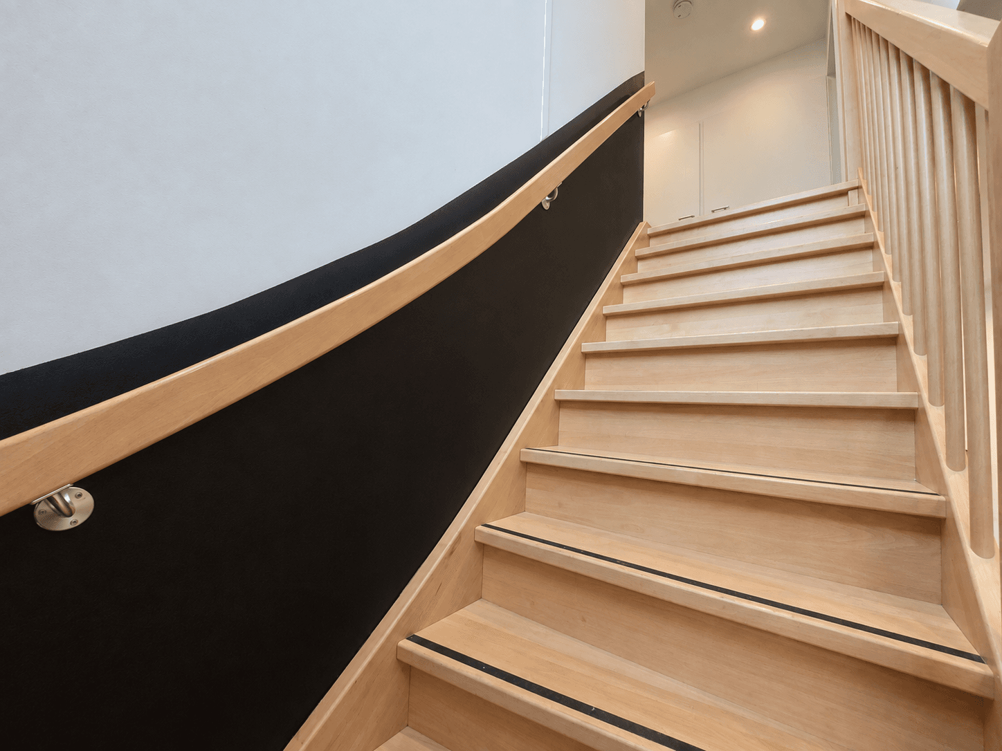 Houten trap met lichte treden en zwart afgeronde leuning, leidt naar de bovenverdieping van de recreatiewoning.