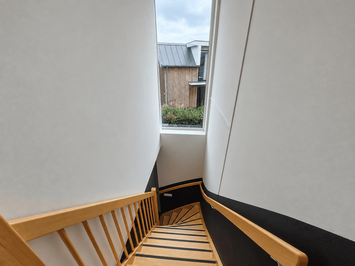 Trap met houten leuning en raam aan de bovenkant, zicht op de buitenruimte van de recreatiewoning