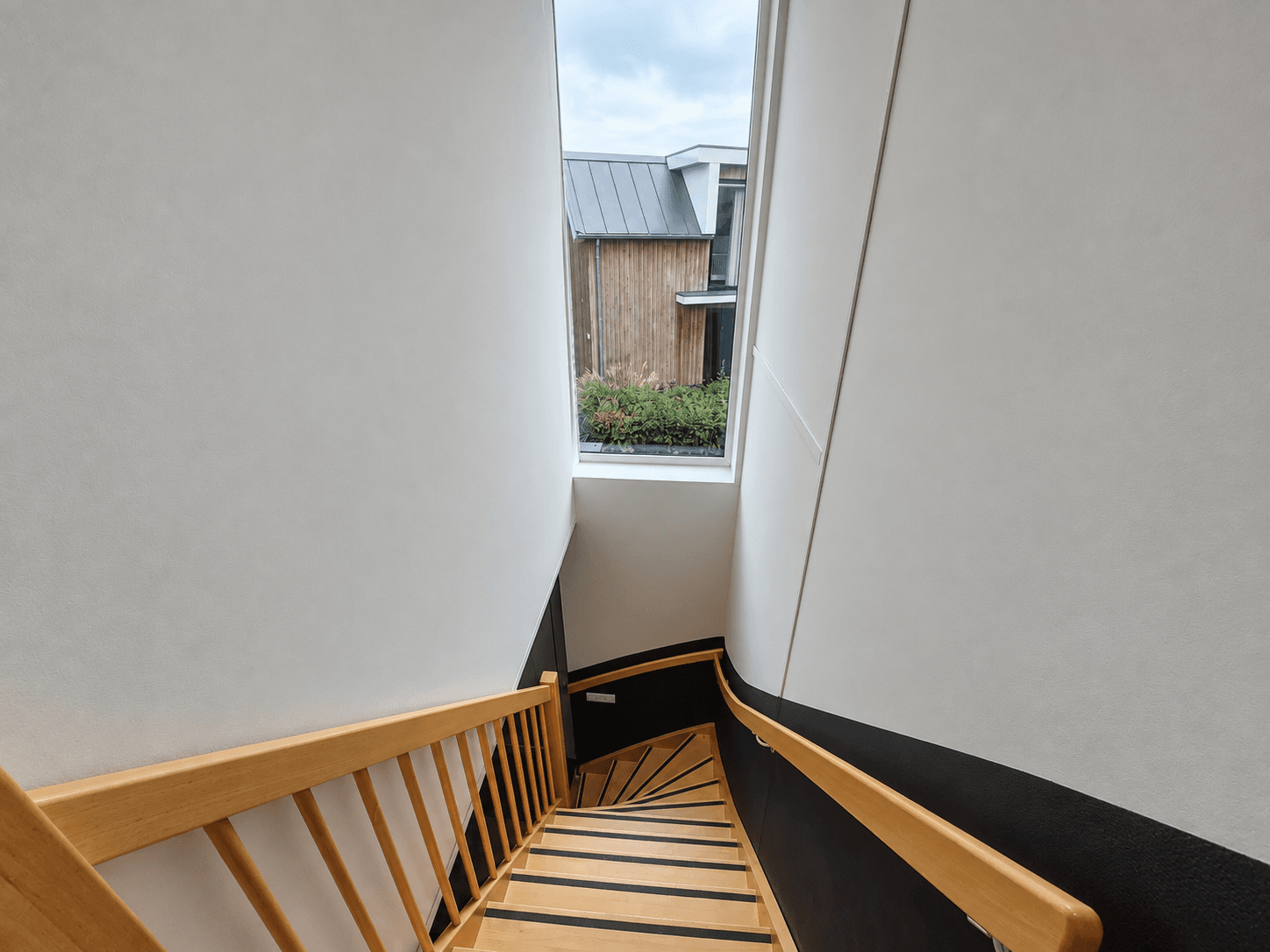 Trap met houten leuning en raam aan de bovenkant, zicht op de buitenruimte van de recreatiewoning