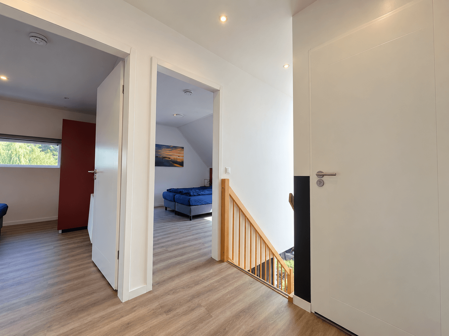 Ingang naar een recreatiewoning met een trap, gang en een slaapkamer zichtbaar. Houten vloer en moderne afwerking.