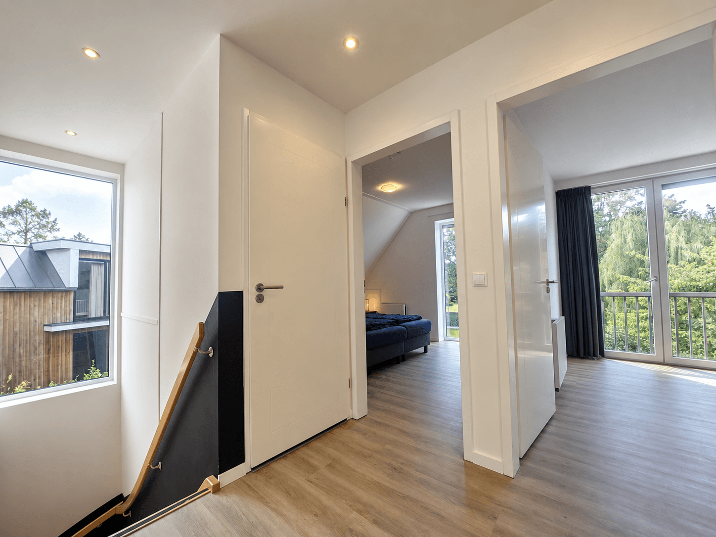 Lichte gang met trappenhuis naar beneden, toegang tot slaapkamers en uitzicht op groene omgeving door groot raam