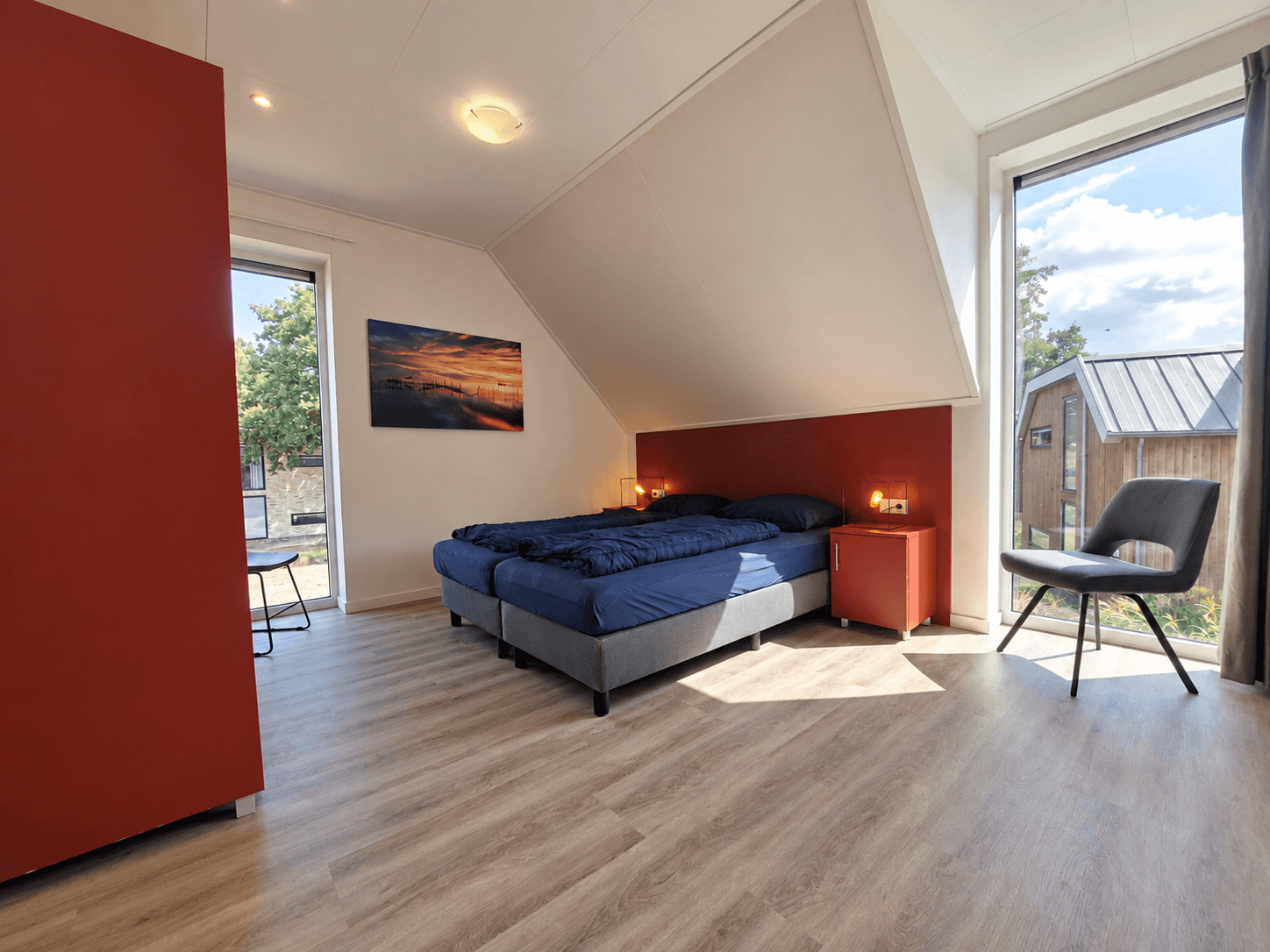 Slaapkamer met twee losse bedden, grote ramen en een moderne inrichting met een fauteuil en avondverlichting.